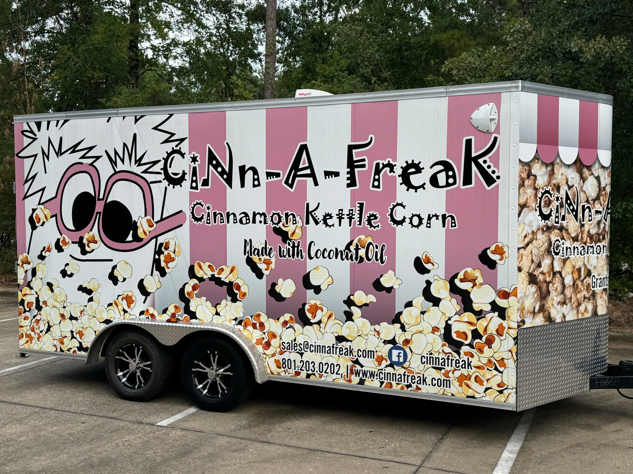Food truck with pink and white stripes, cartoon character, and popcorn graphics, advertising cinnamon kettle corn, parked outdoors.
