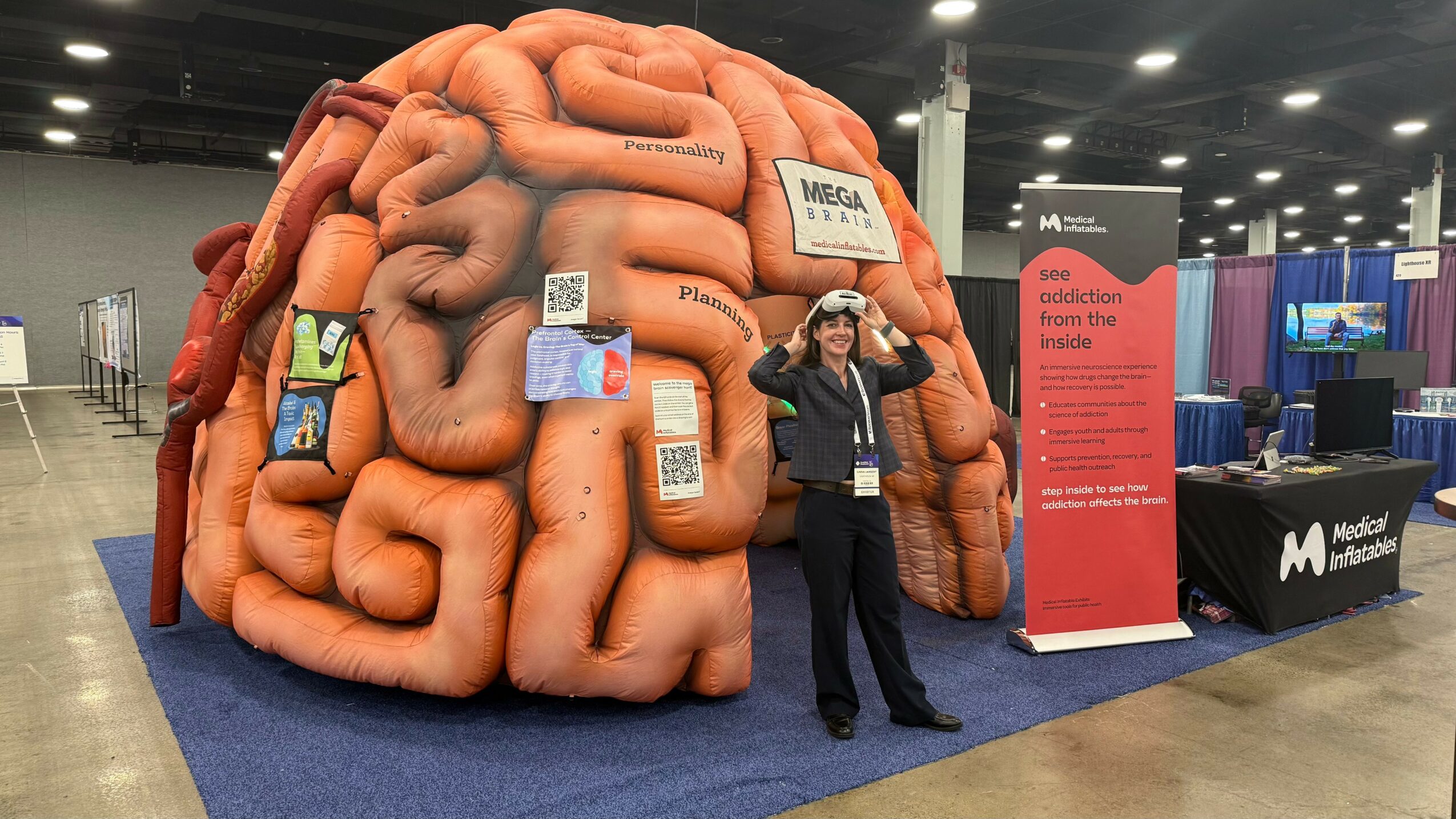 Person standing in front of a large, colorful model of intestines at an indoor exhibition. Booths and banners are visible.
