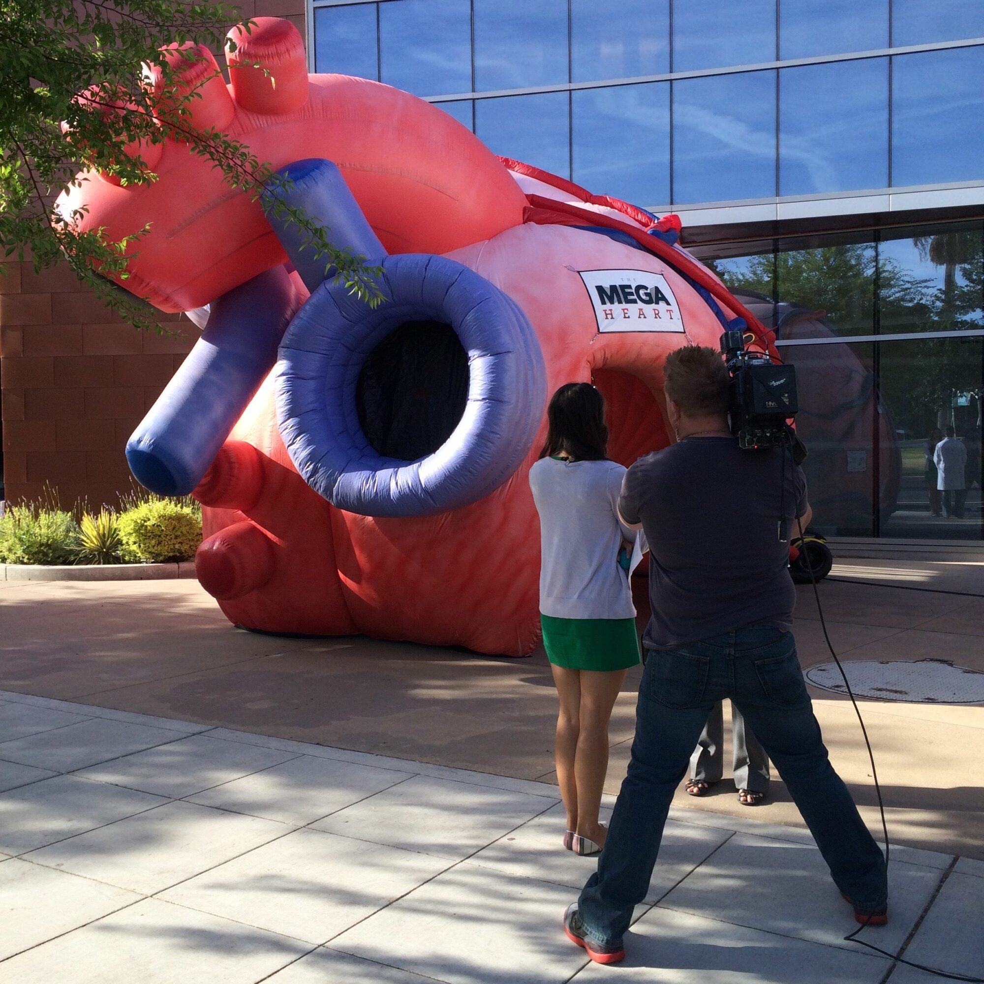Two people stand near a large red inflatable structure outdoors, with a glass building in the background.