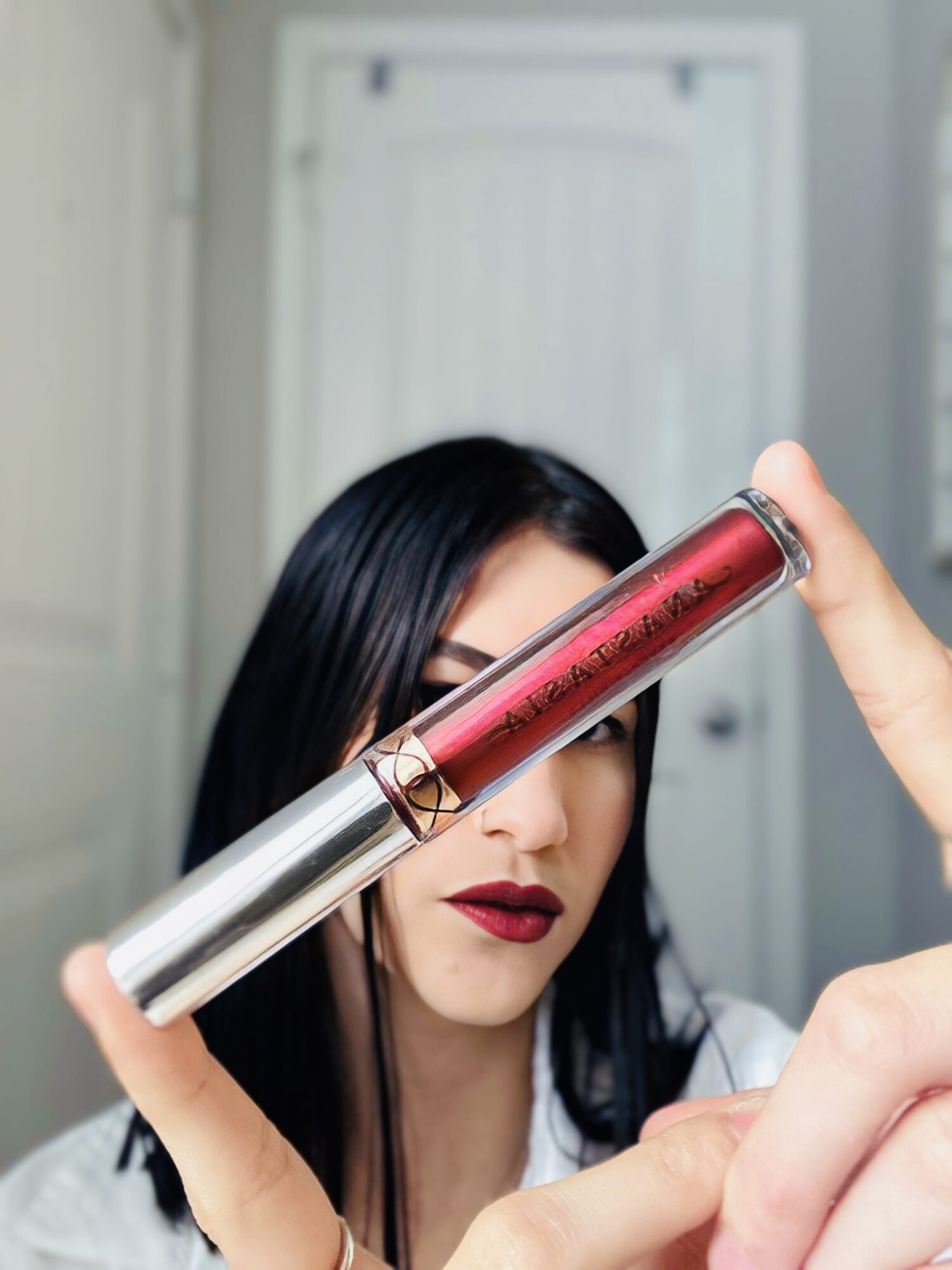 Woman with dark hair and red lipstick holding a lipstick tube in front of her face indoors.