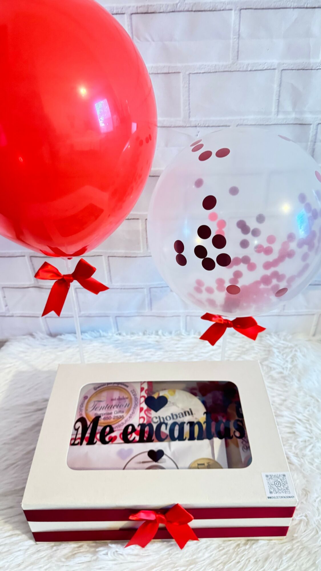 Two balloons, one red and one transparent with confetti, with red bows, and a gift box with a message inside.