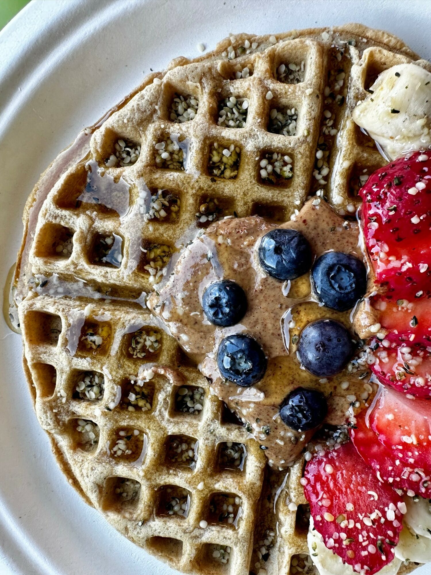 Two waffles topped with blueberries, banana slices, and strawberries, served with whipped cream on a white plate.
