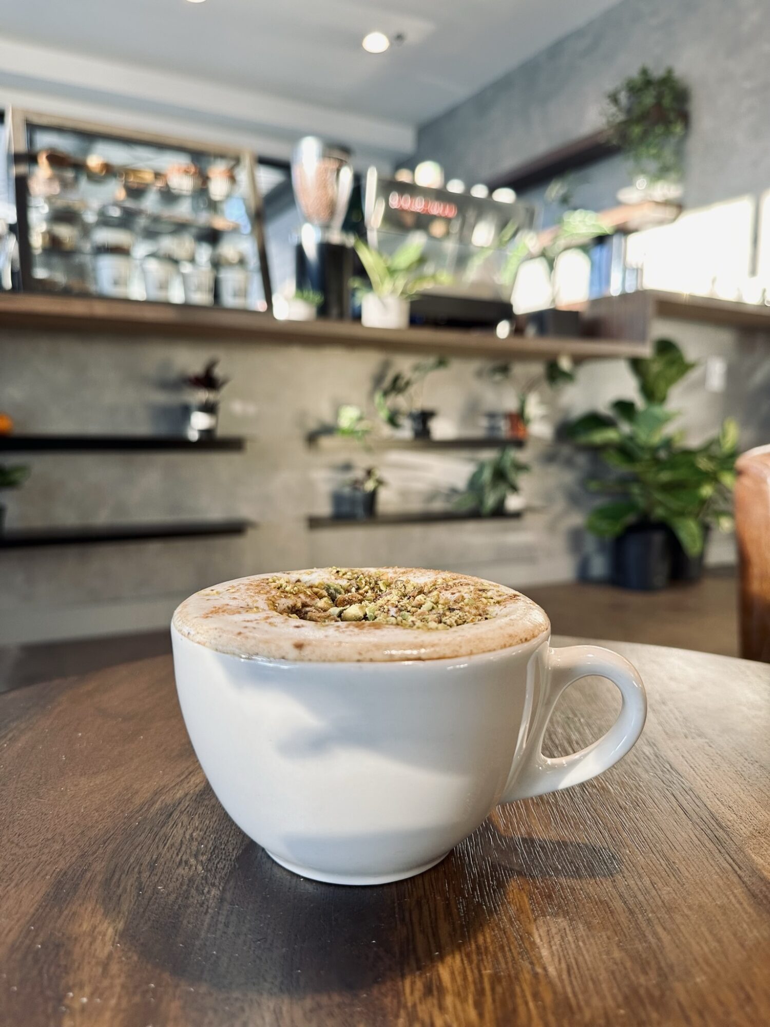 White cup of frothy coffee on a wooden table with a cafe interior in background.
