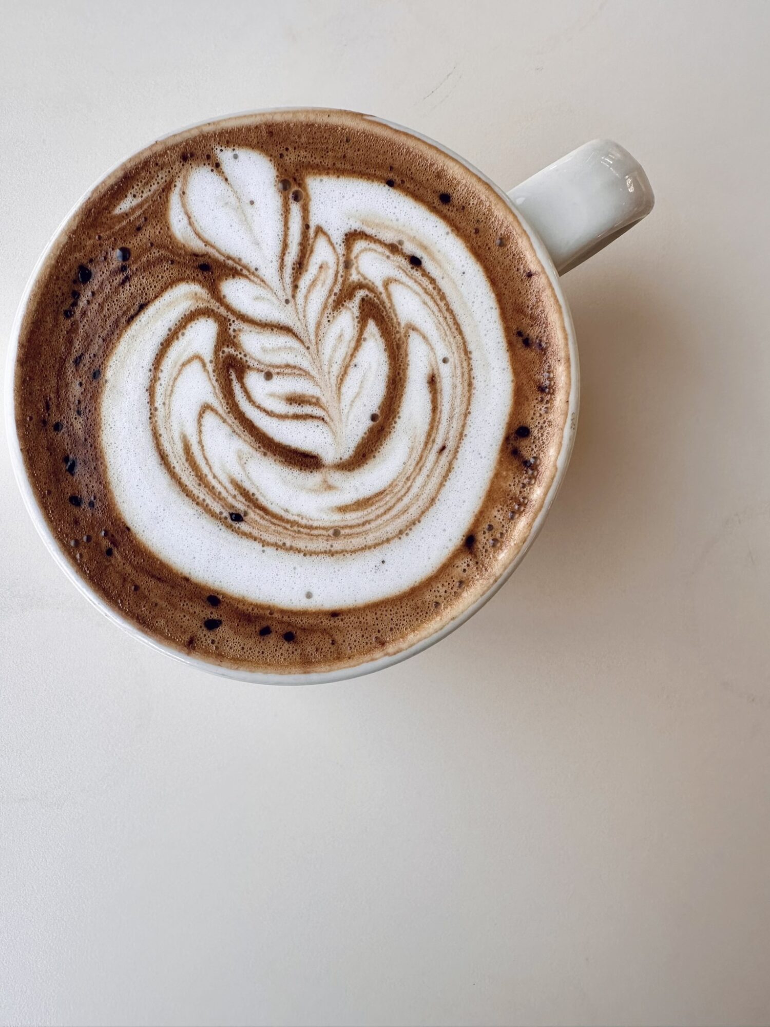 Top view of a coffee cup with latte art on a white surface.