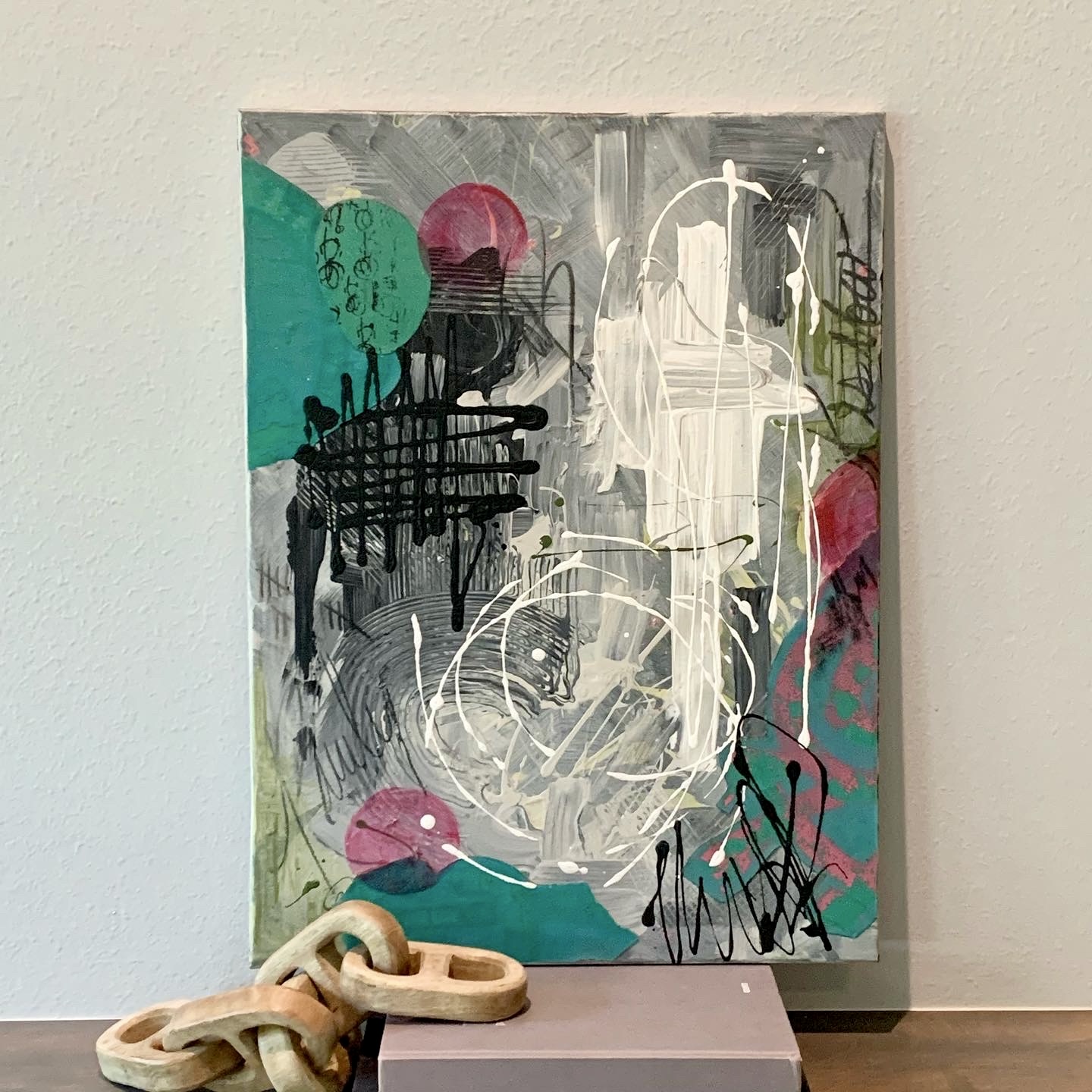 Abstract painting with colorful shapes, black and white lines, and pink, green, and teal accents on a canvas.