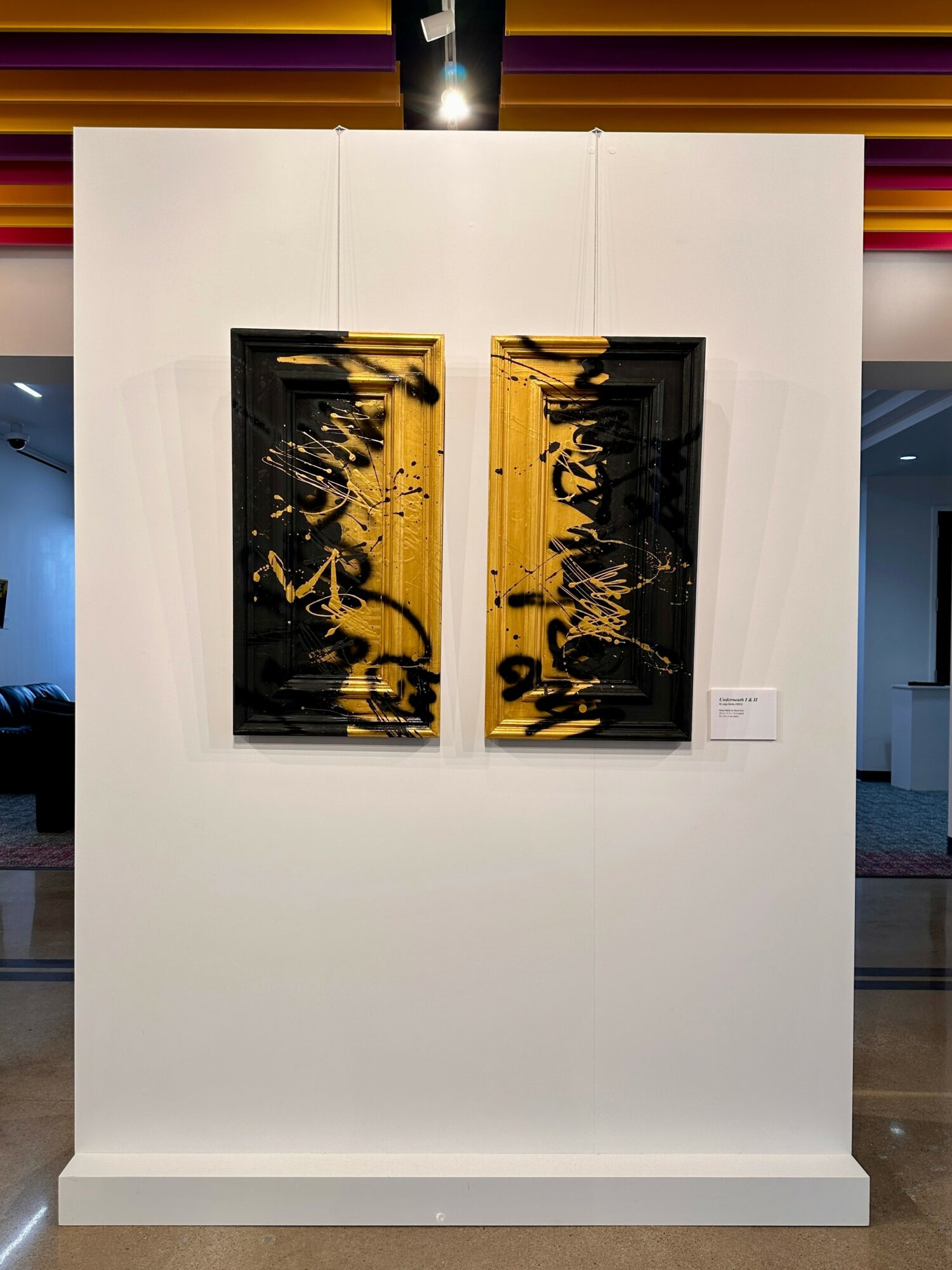 Two abstract paintings with black and yellow designs on a white wall, displayed side by side.