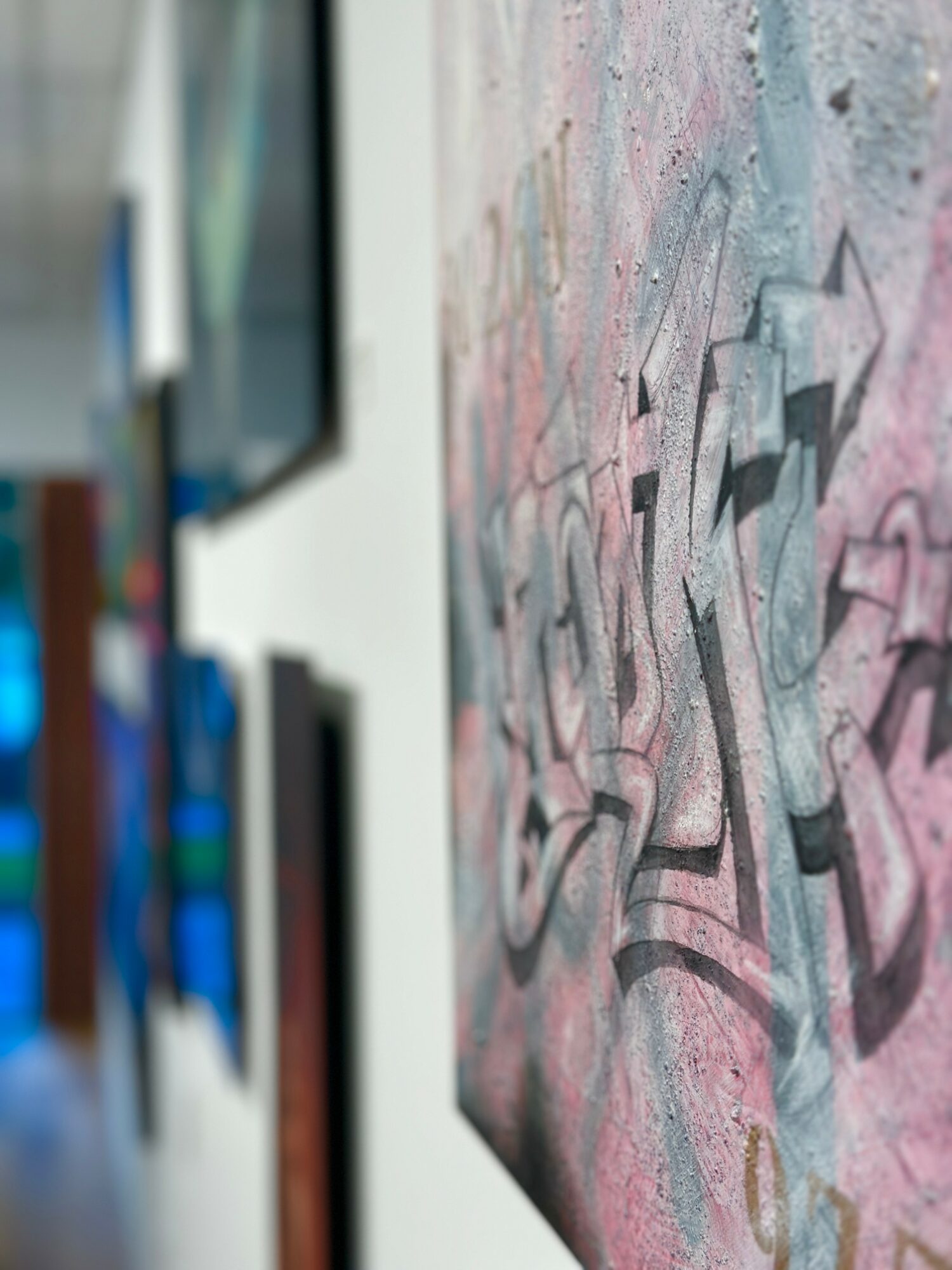Close-up of graffiti on a wall with pink, blue, and gray colors, with blurred background.