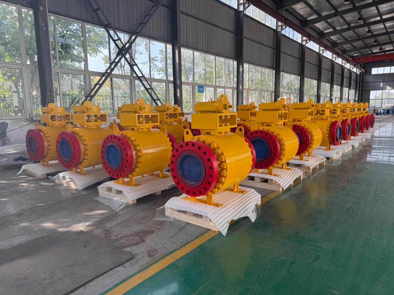 Multiple yellow industrial valves with red and blue details lined up inside a warehouse, on white pallets.