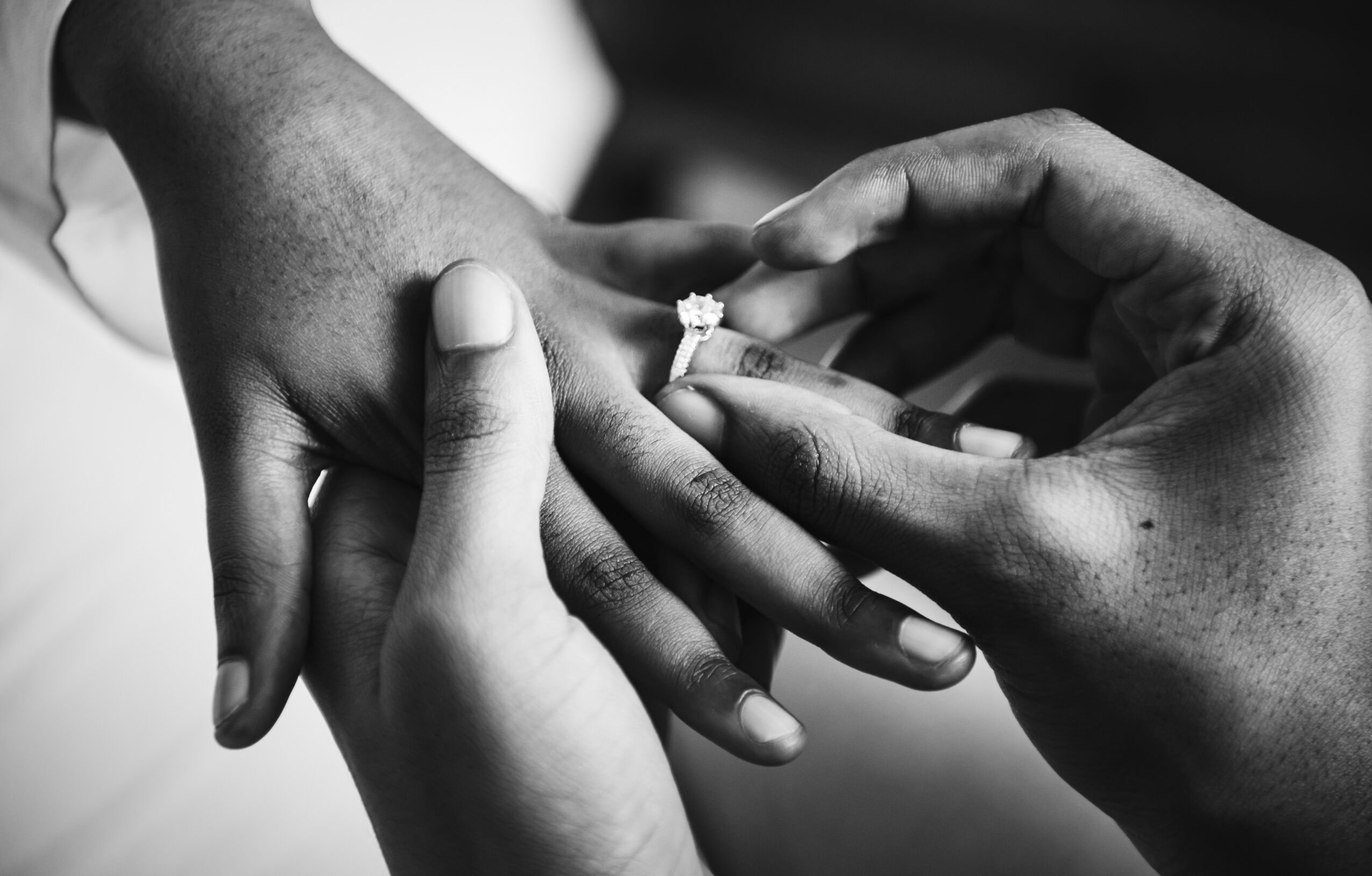 Person placing a ring on another person's finger, close-up of hands, black and white image.