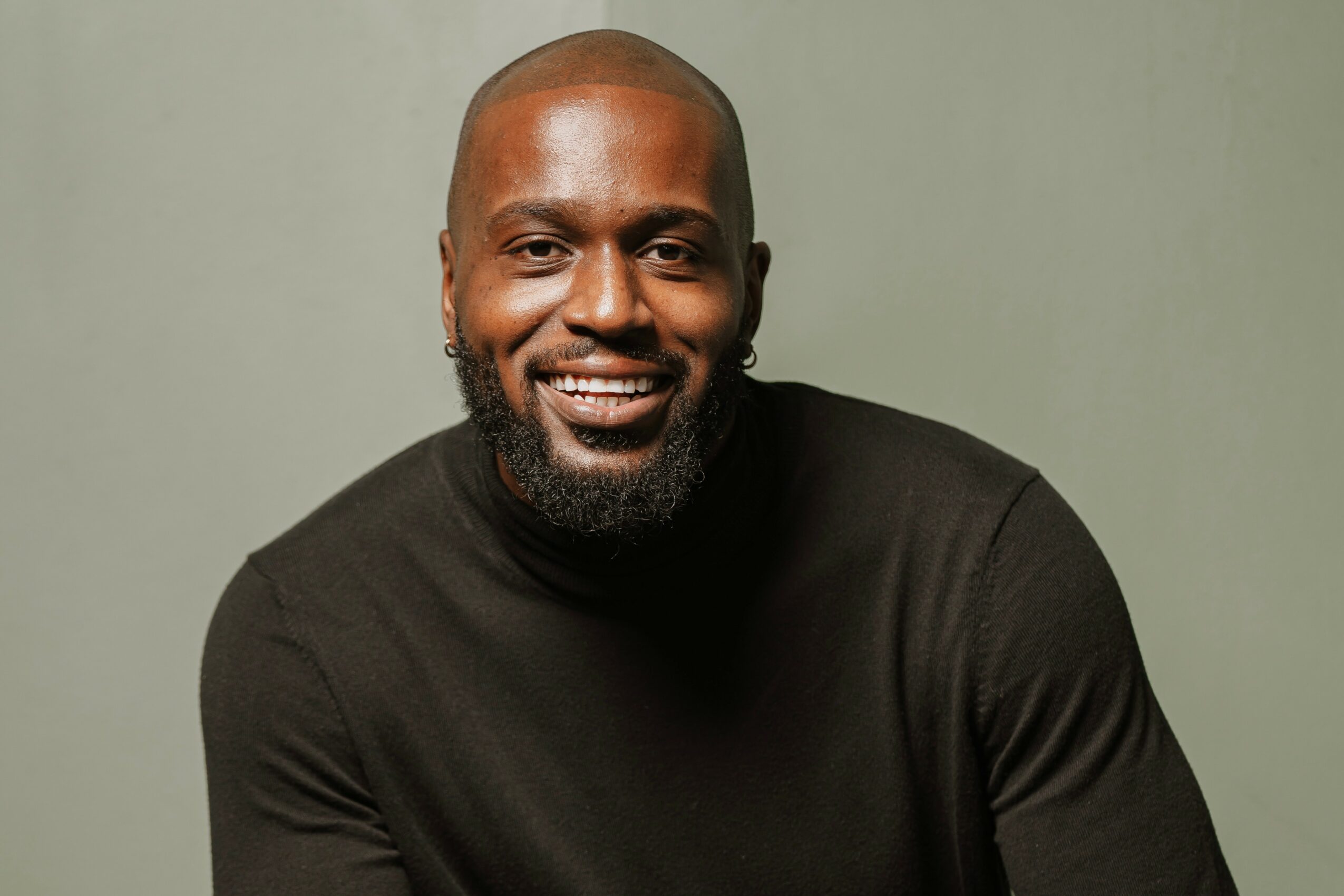 A smiling man with a beard wearing a black shirt against a plain background.