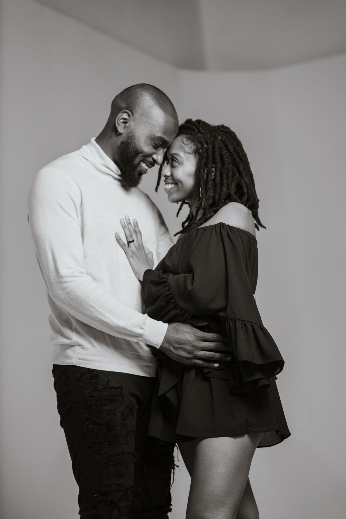Two people smiling and embracing, facing each other closely, in a black and white photo.