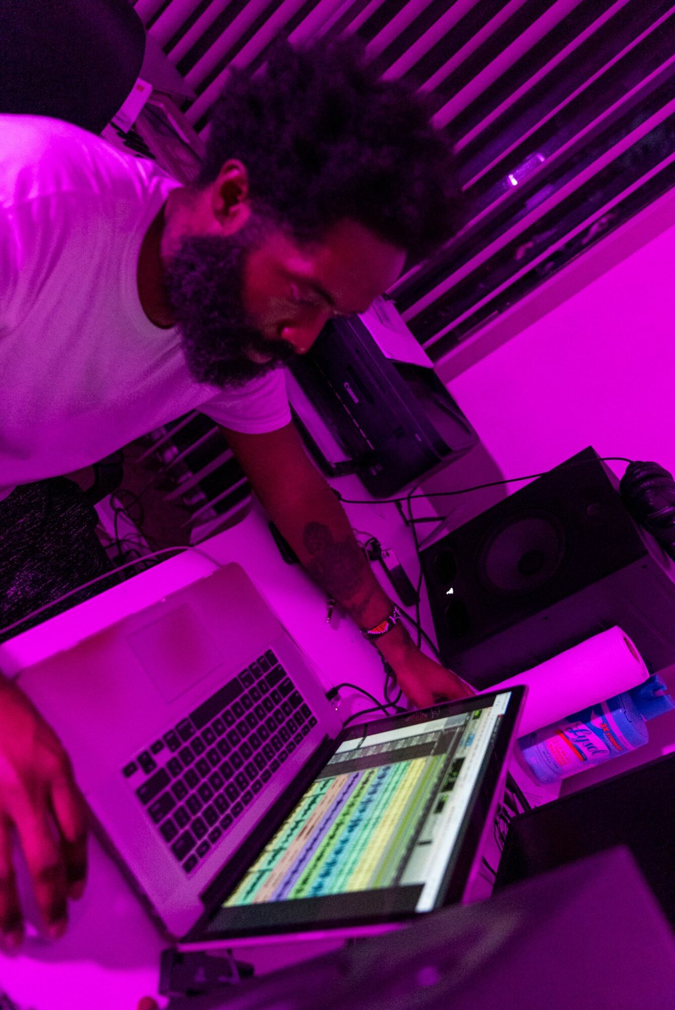 Person working on music production with a laptop and audio equipment, illuminated by purple lighting.