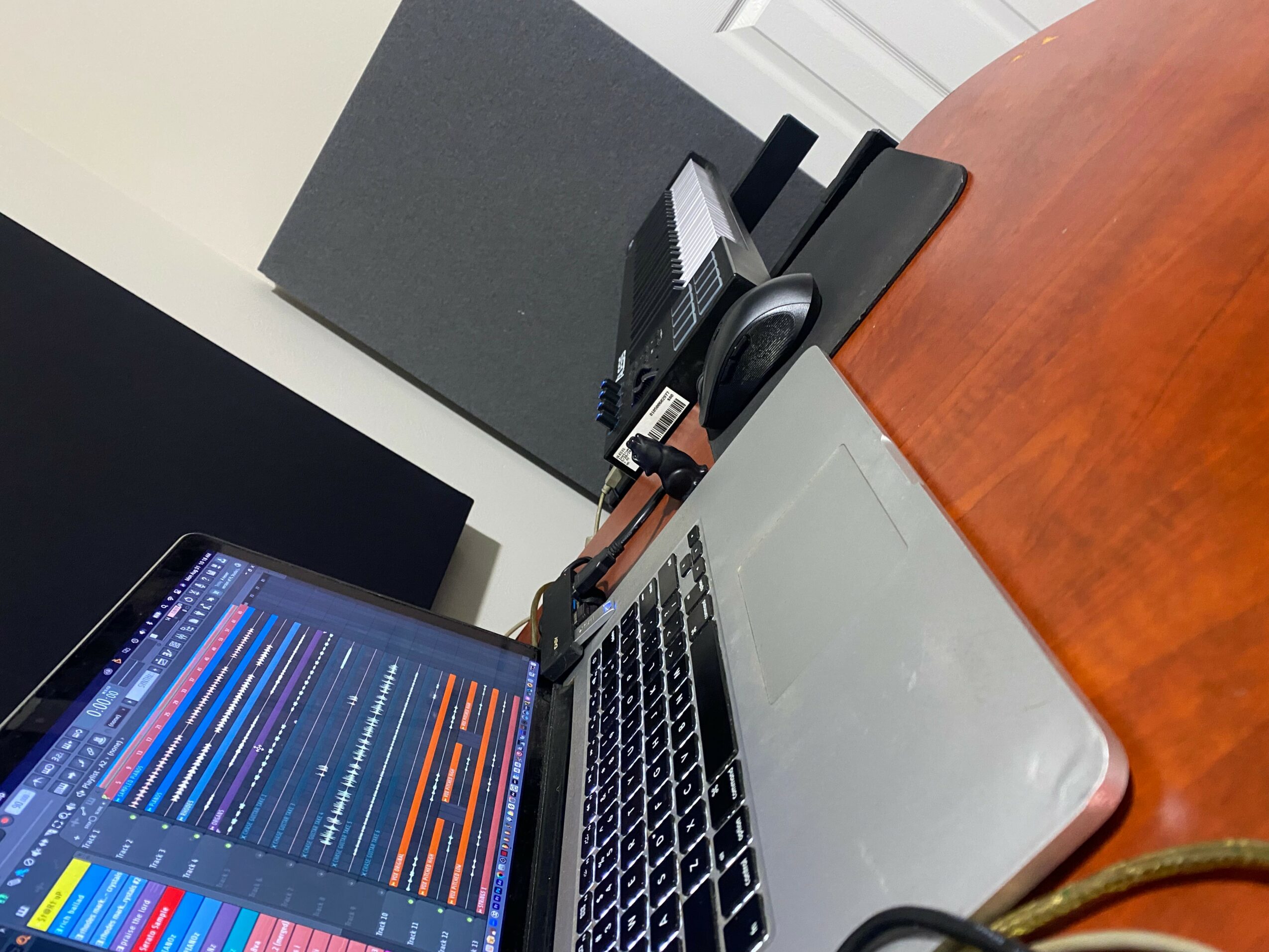 Laptop on a wooden desk displaying a colorful music mixing interface, with a phone and office supplies nearby.