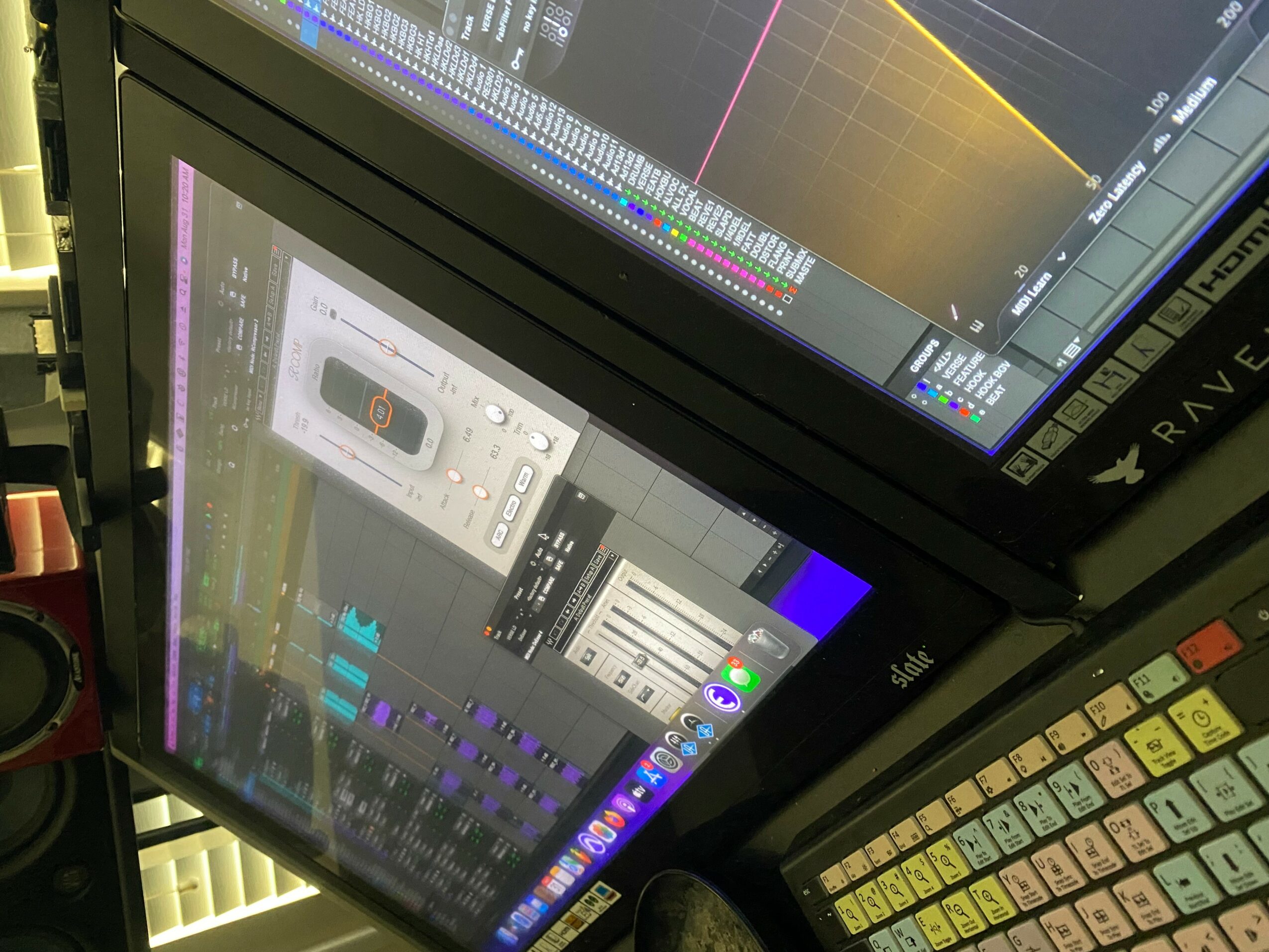 Two computer screens displaying audio editing software, with a colorful keyboard visible in the foreground.