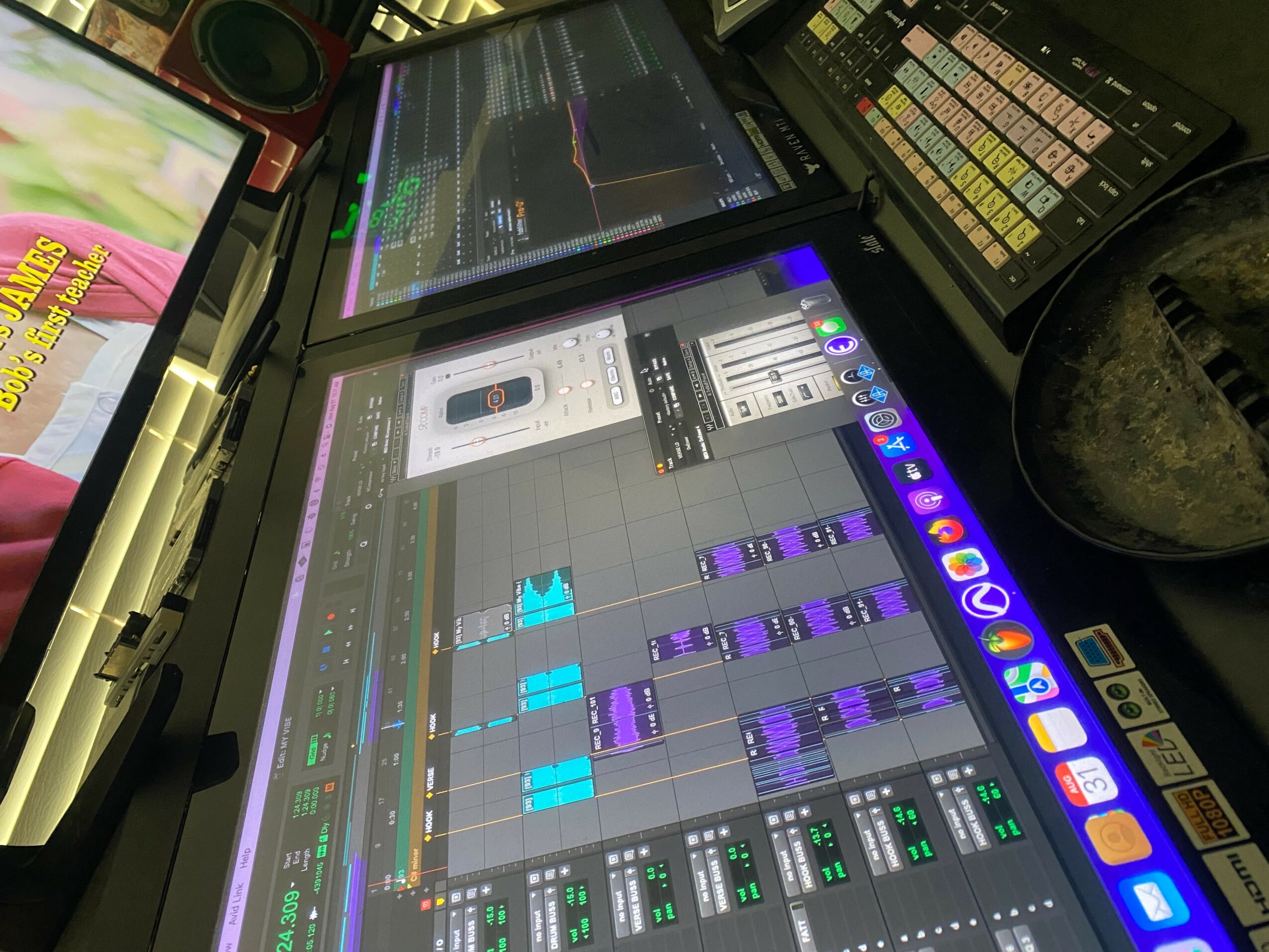 Music production software on a laptop screen with audio tracks and controls, surrounded by other electronic devices.