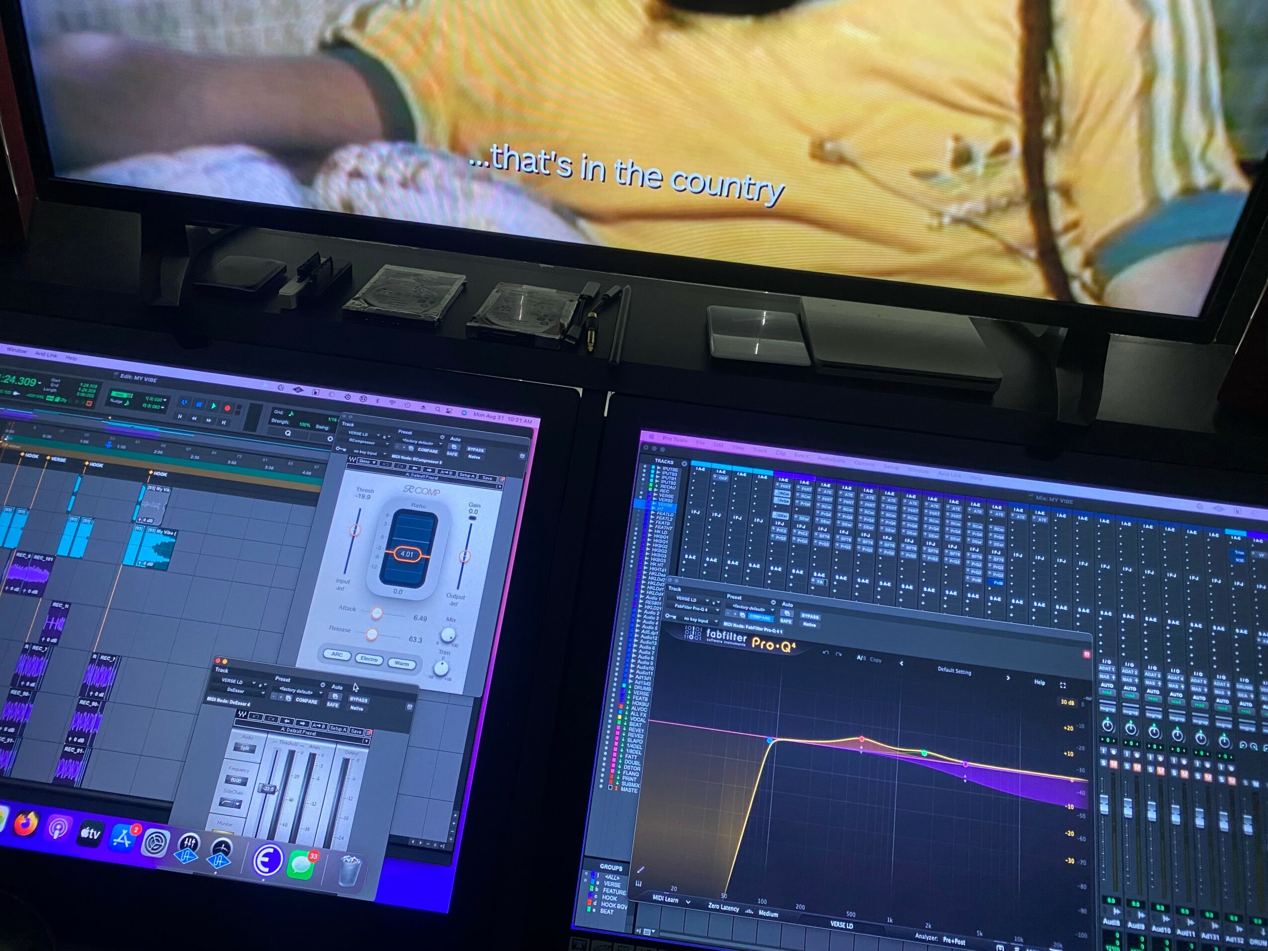 Two computer screens displaying audio editing software and a television screen showing a person in a yellow shirt.