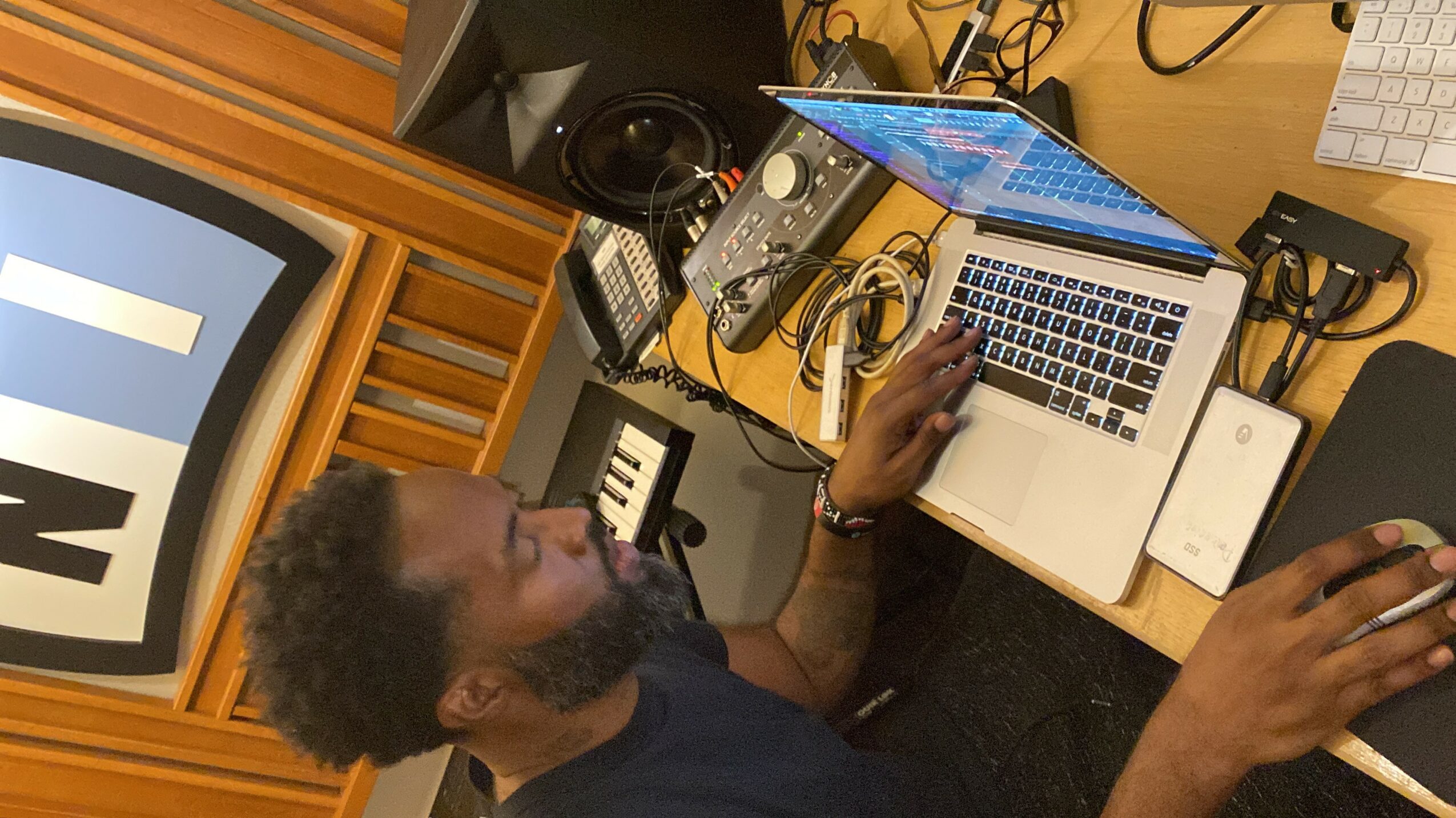 Person working at a music studio with a laptop, keyboard, and audio equipment, viewed from above.