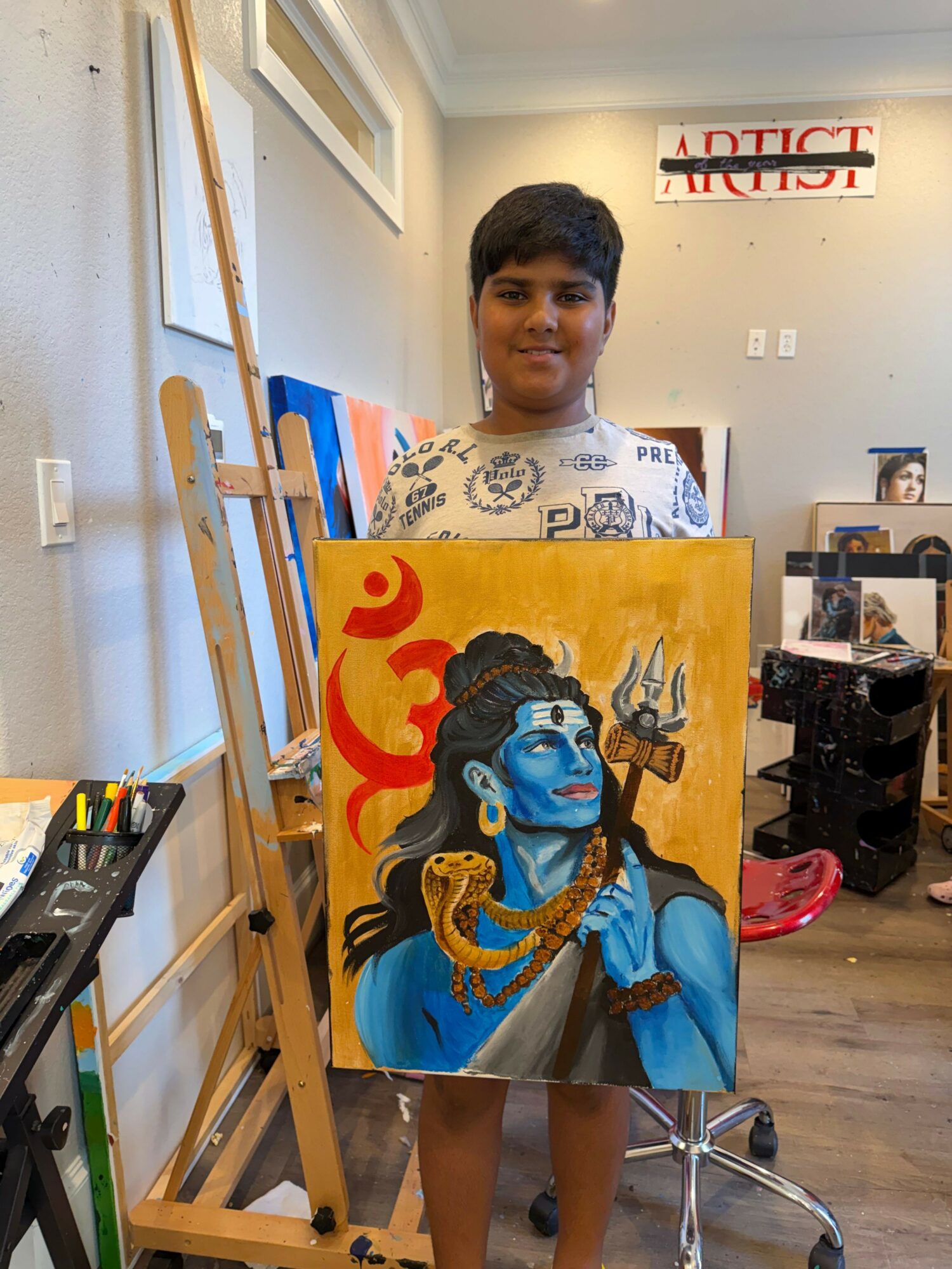 Person standing next to an easel with a colorful painting of a woman with blue skin and jewelry, in an indoor space.