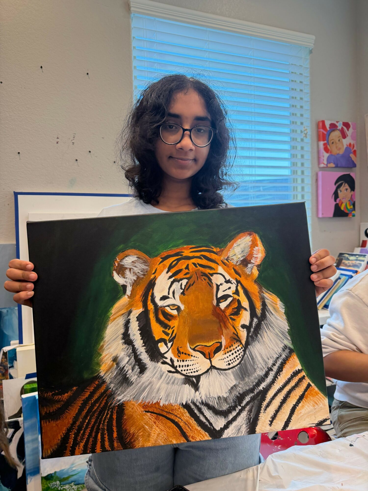 Person holding a painting of a tiger's face with orange, black, and white stripes, and green background.