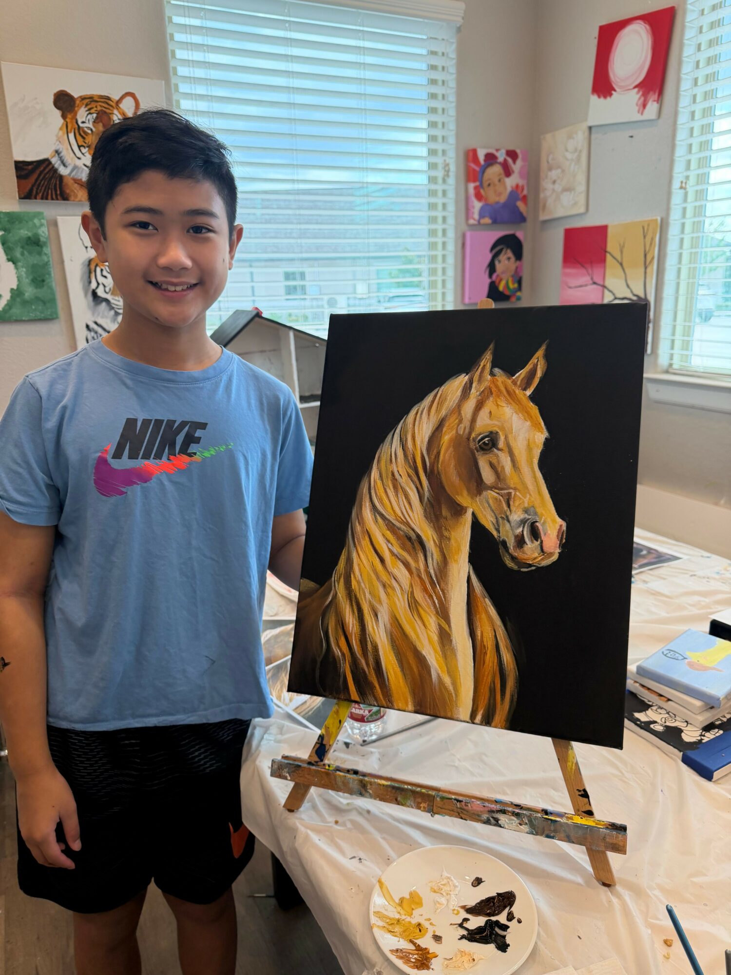 Young woman painting a horse on a black canvas in a bright room with large windows.