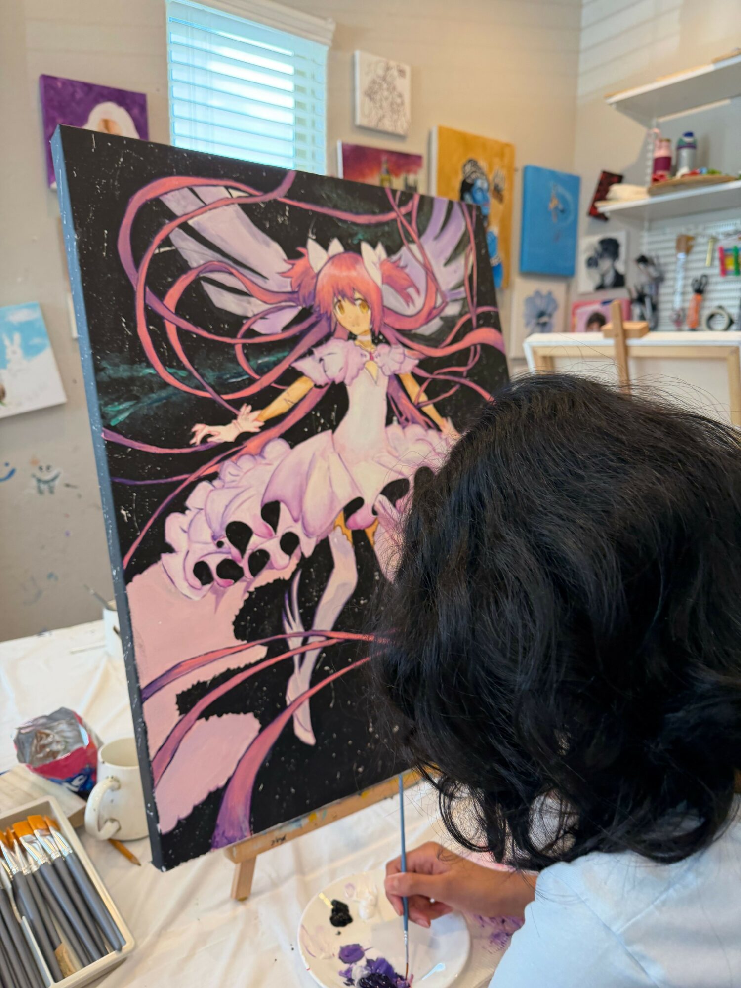 Person painting a large canvas with a colorful abstract design, using a brush, in a room with art supplies and colorful decorations.