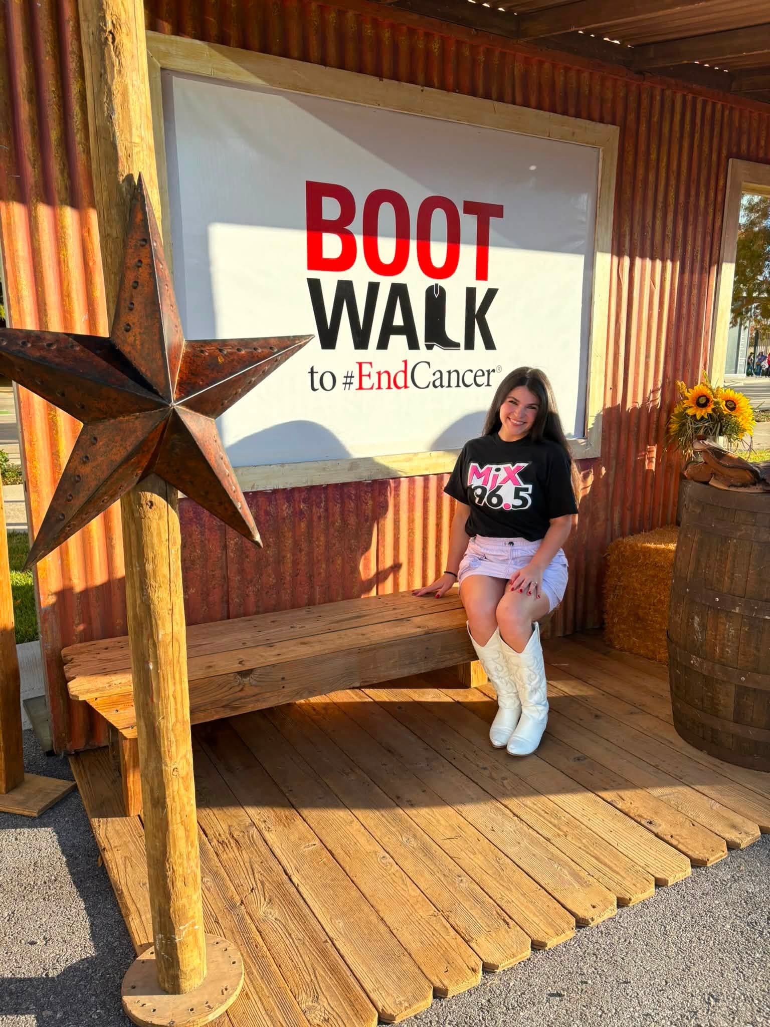 Young girl sitting on a wooden bench in front of a sign supporting cancer awareness, with a star decoration nearby.