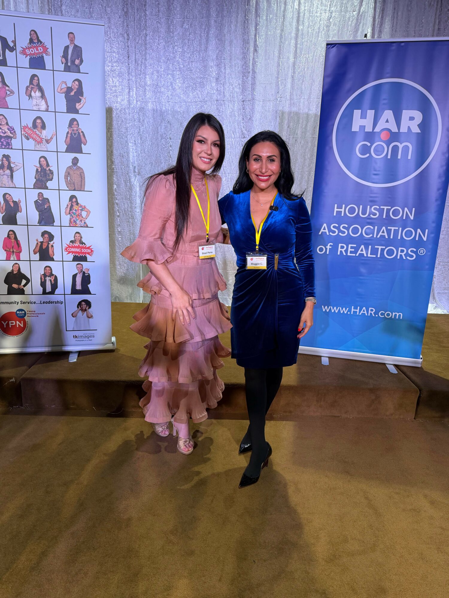 Two women standing together at an event, smiling, with a HAR.com banner and photo display in the background.