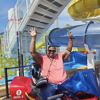 Person with arms raised at water park, colorful slides and structures in background.