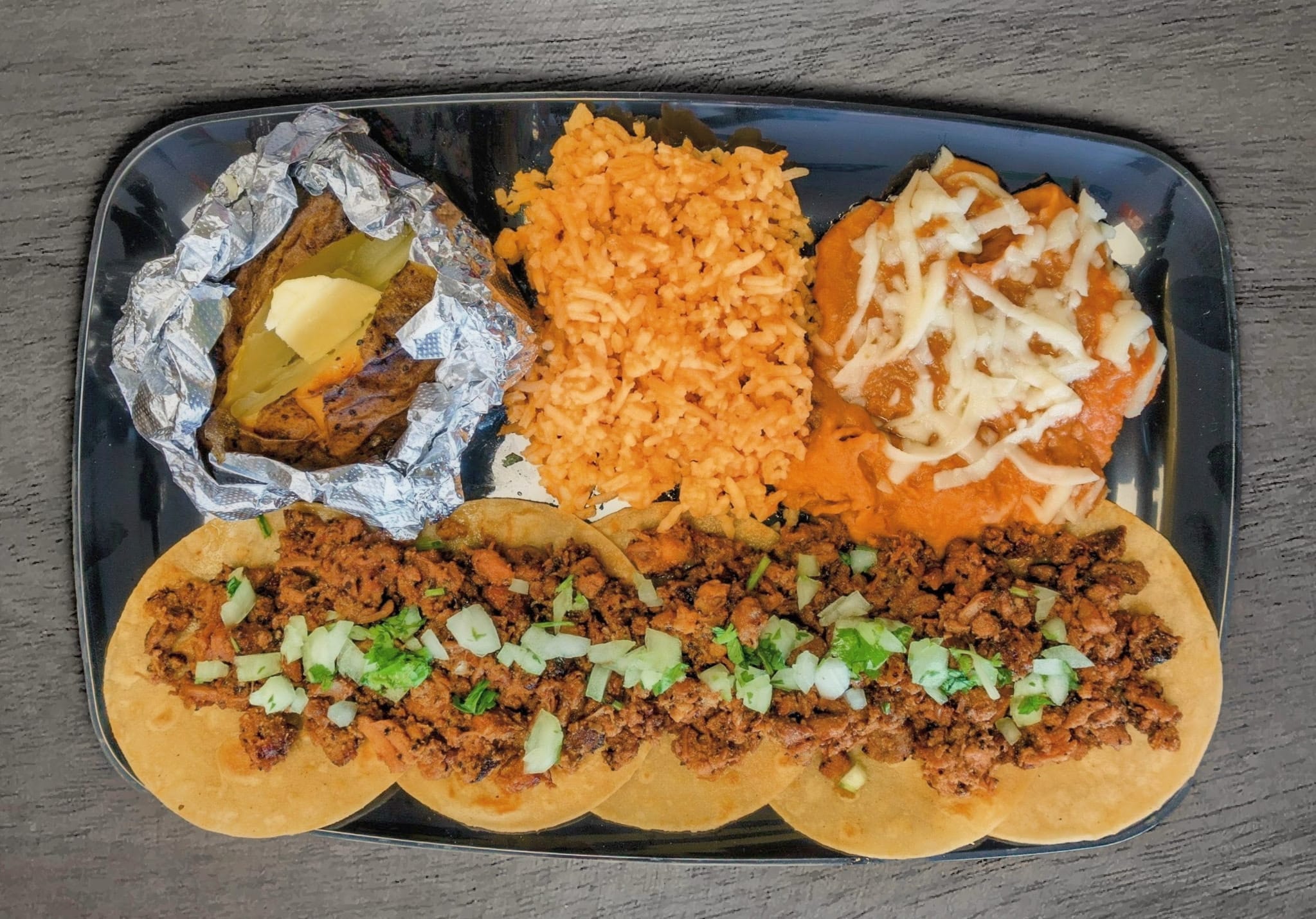 Tray with baked potato, rice, chili cheese fry, and a hot dog with chopped onions and sauce.