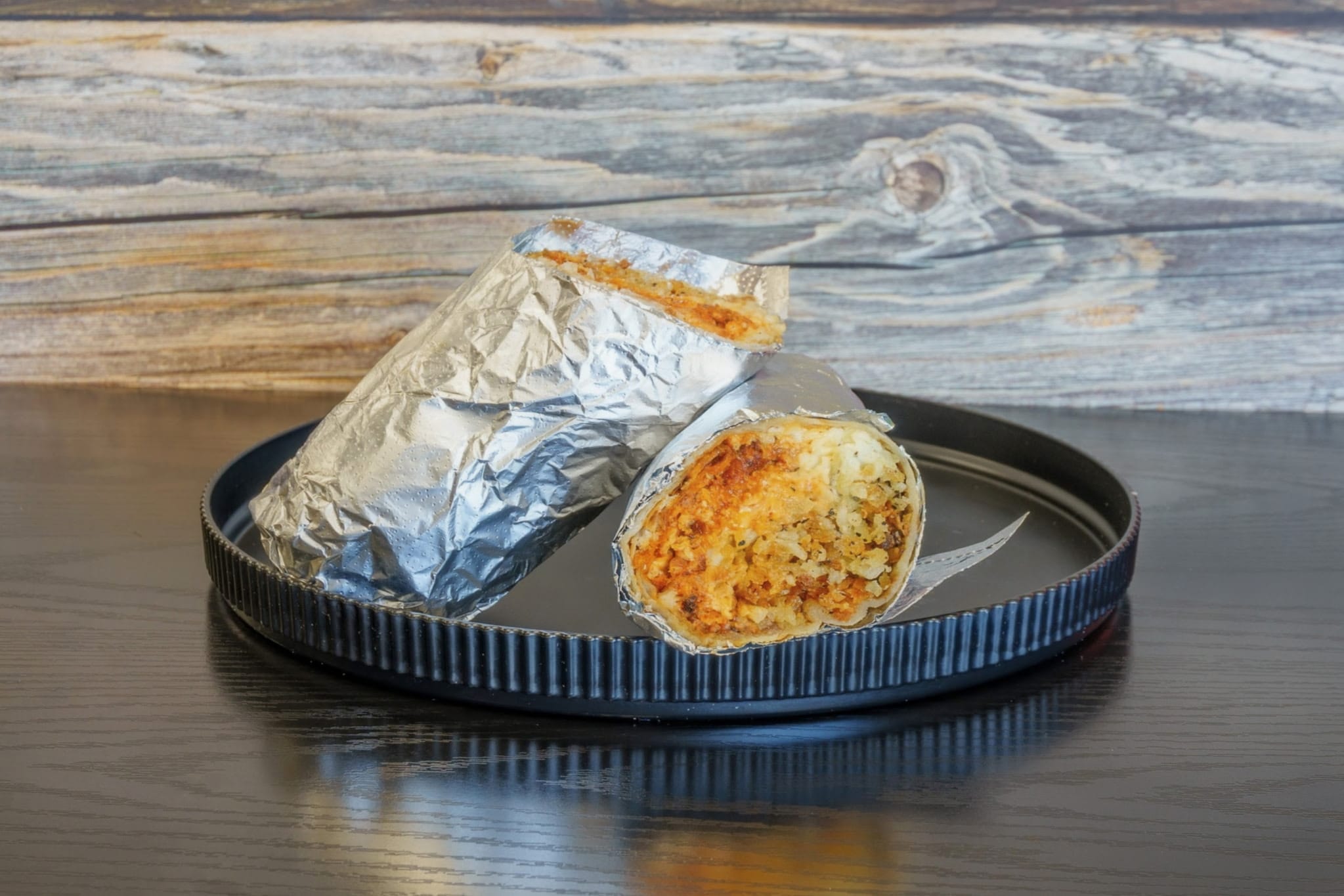 Wrapped food item with a cut open section revealing filling, on a black tray against a wooden background.