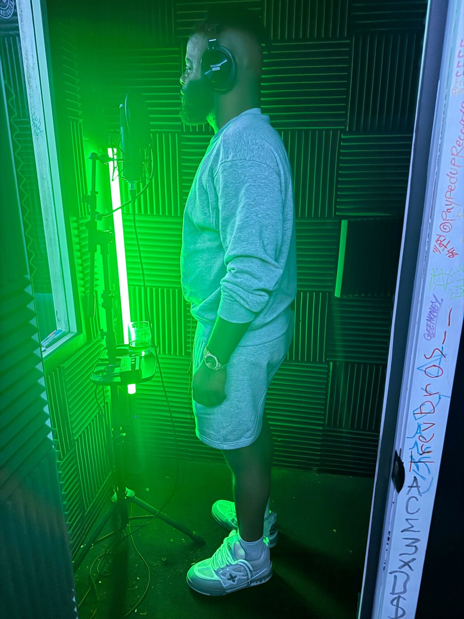 Person standing in a room with green lighting, wearing a hoodie, shorts, and sneakers, facing sideways.