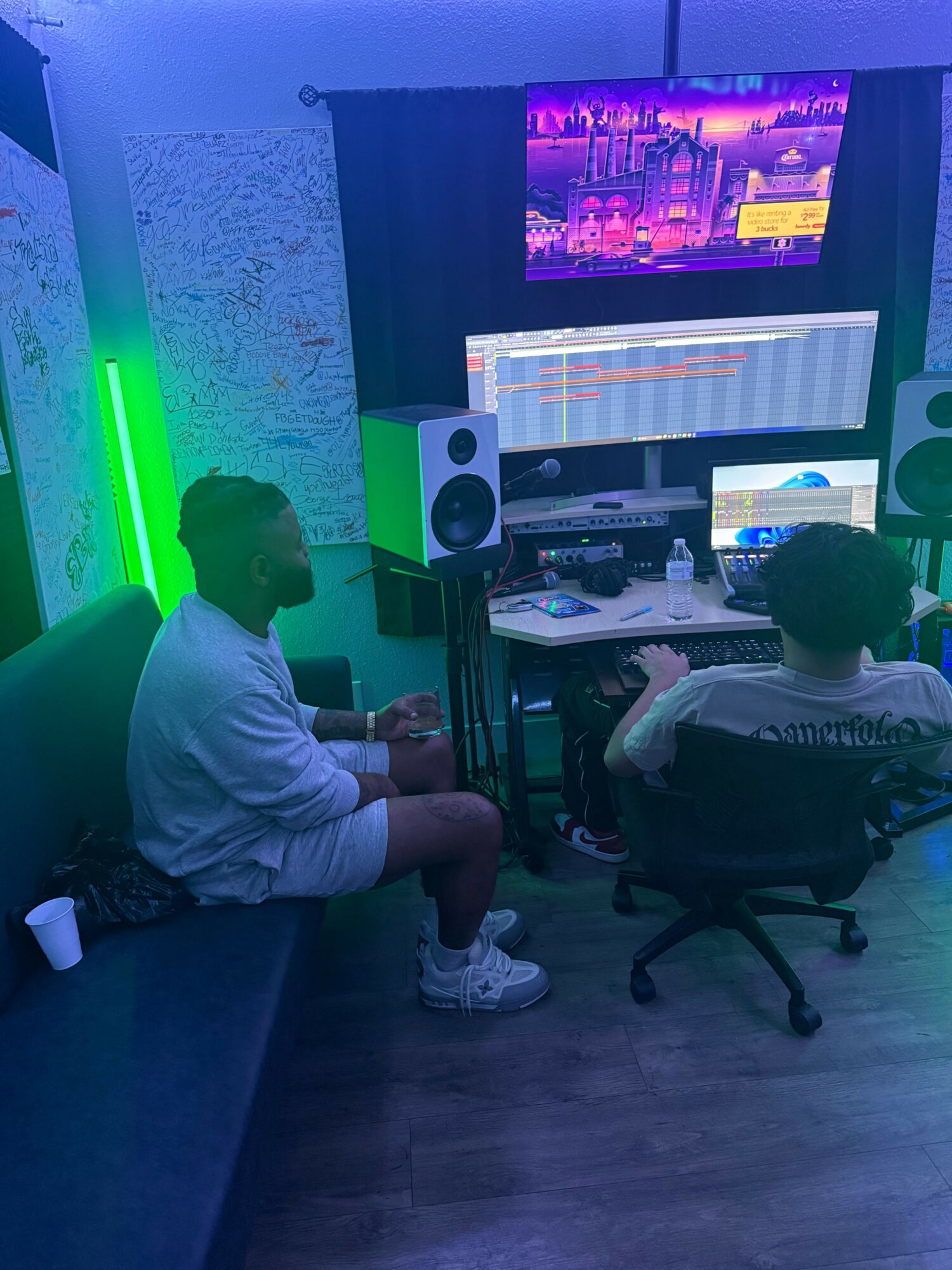 Child sitting on a couch in a music studio with computer screens and audio equipment, illuminated by colorful lights.