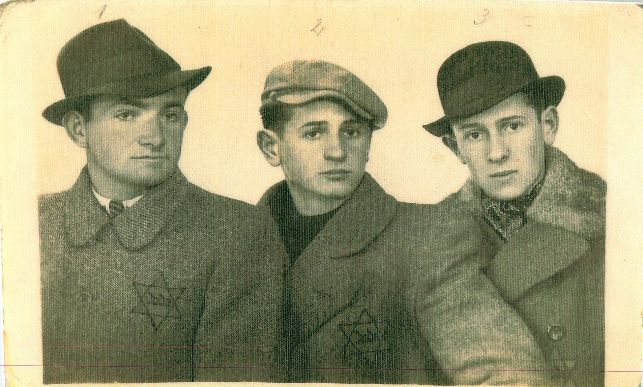 Three boys wearing coats and hats, standing close together, looking at the camera, in black and white.