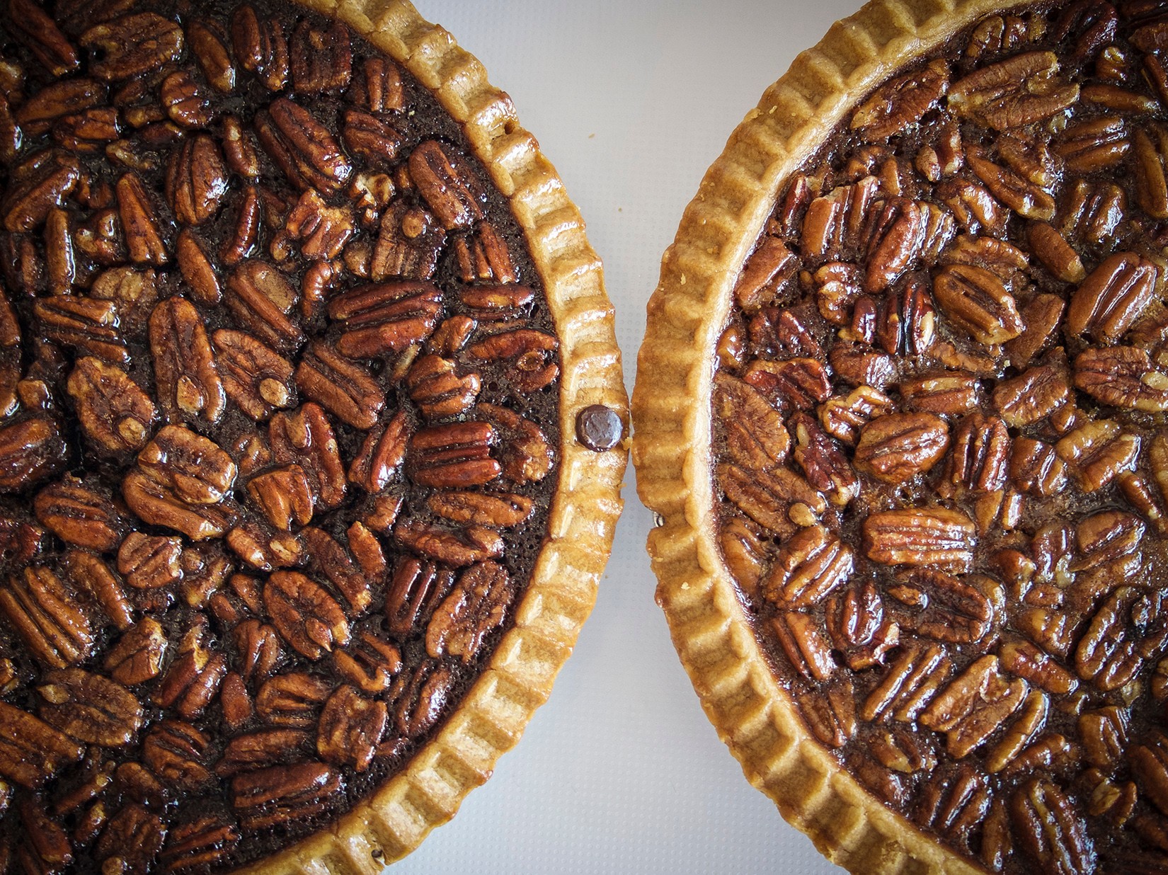Two pecan pies with golden crusts, filled with pecans, placed side by side on a light surface.