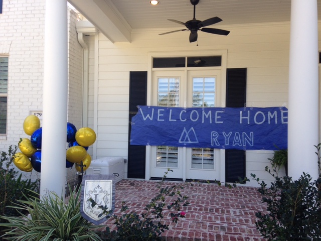 Front porch with a welcome home sign, balloons, and plants, with a door and window in the background.