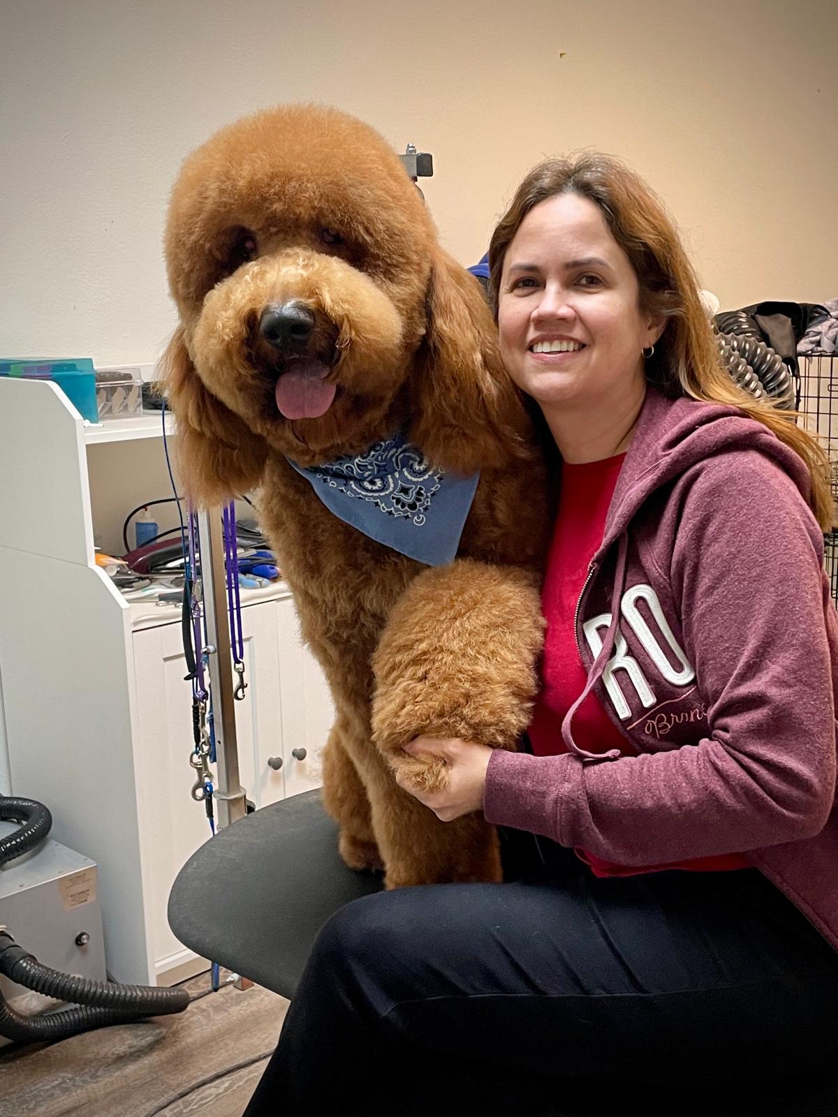 Woman smiling with large, fluffy brown dog wearing a blue bandana, sitting on a chair indoors.