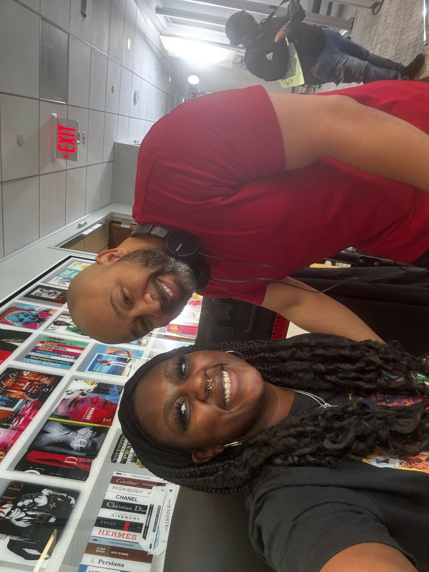 Two women smiling, one with long braids, in a store with shelves of books and DVDs.