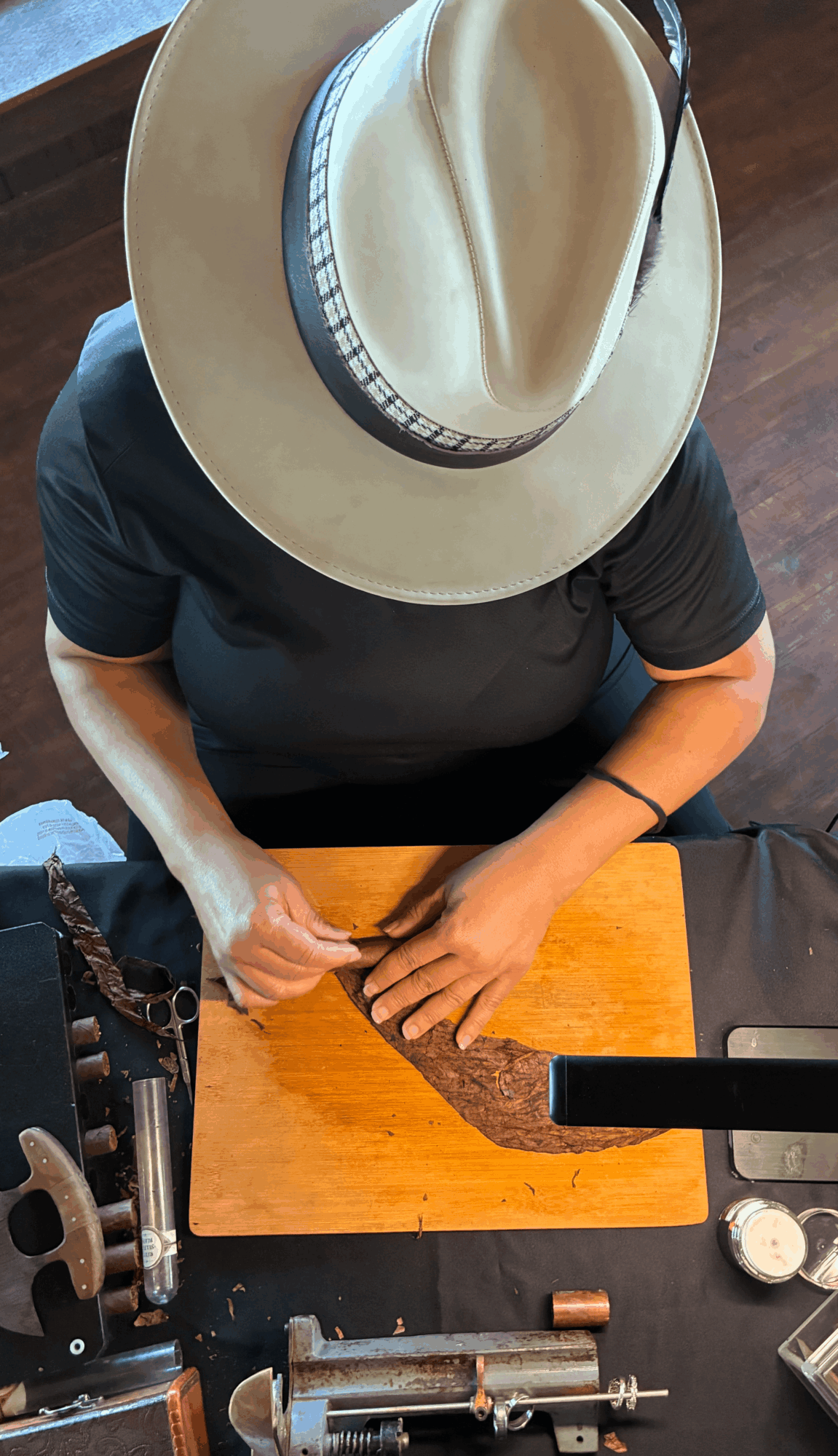 Person wearing a hat and black shirt, working with a tool on a wooden surface, viewed from above.