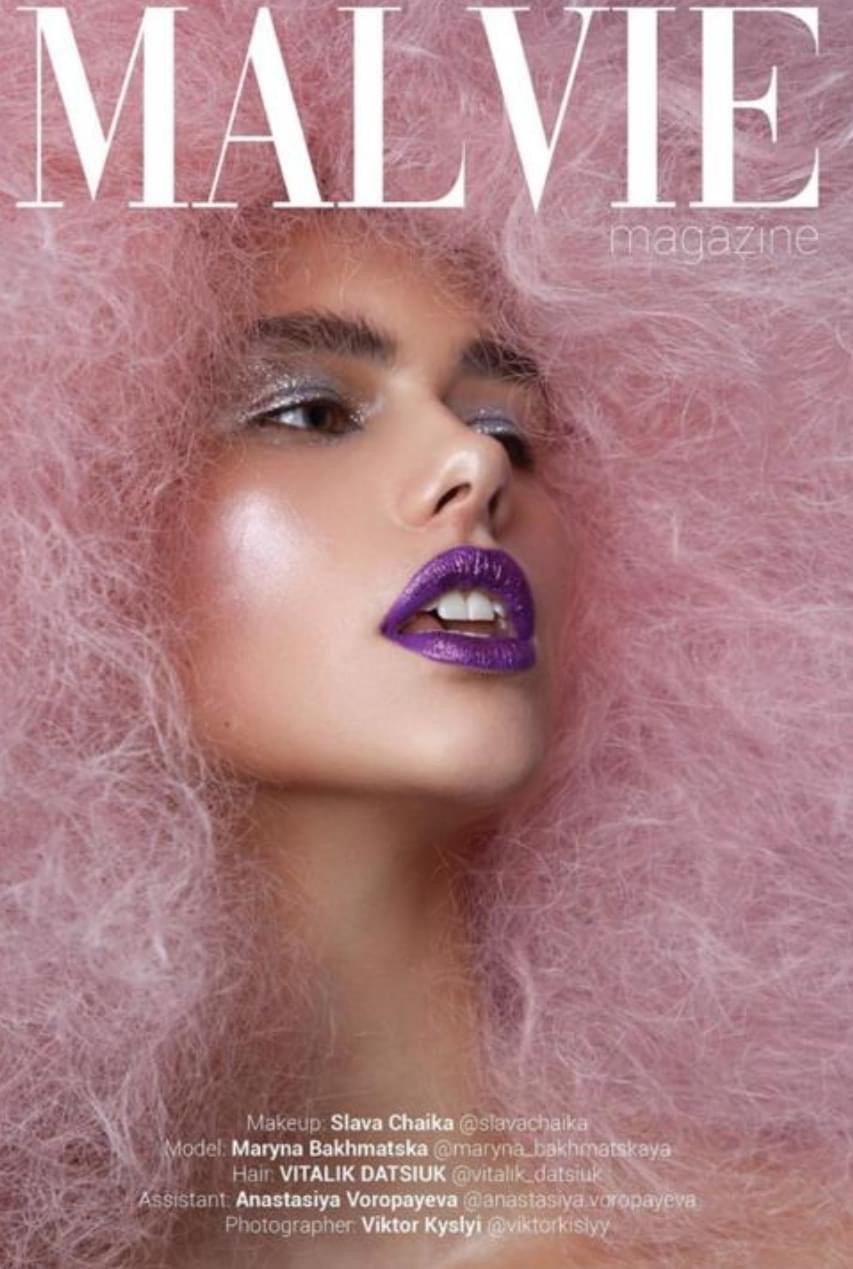 Close-up of a woman with pink hair, purple lipstick, and makeup, looking to the side.