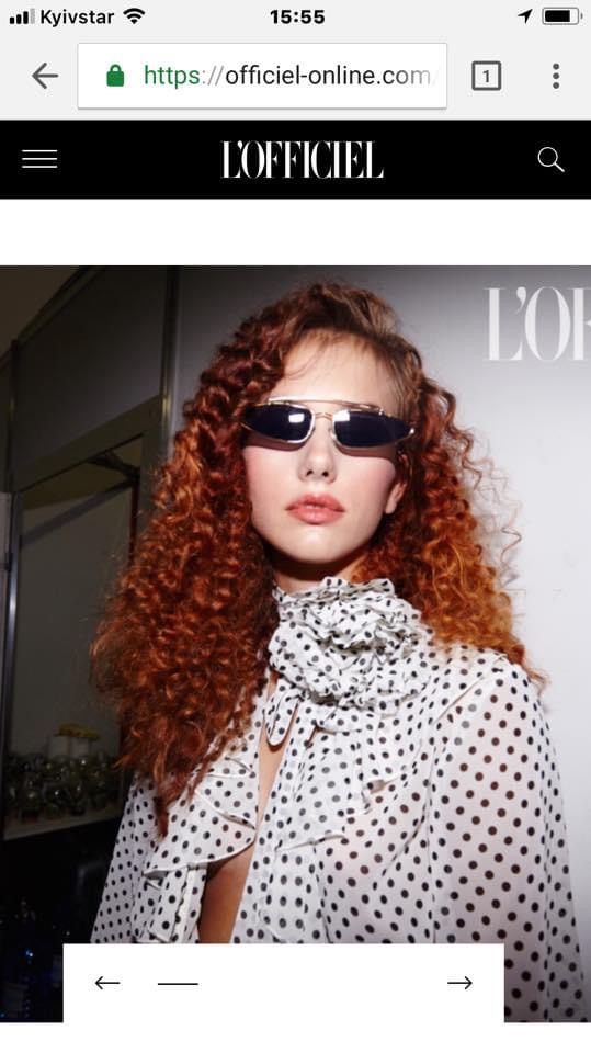 Woman with curly red hair wearing sunglasses and a polka dot blouse, looking at camera.