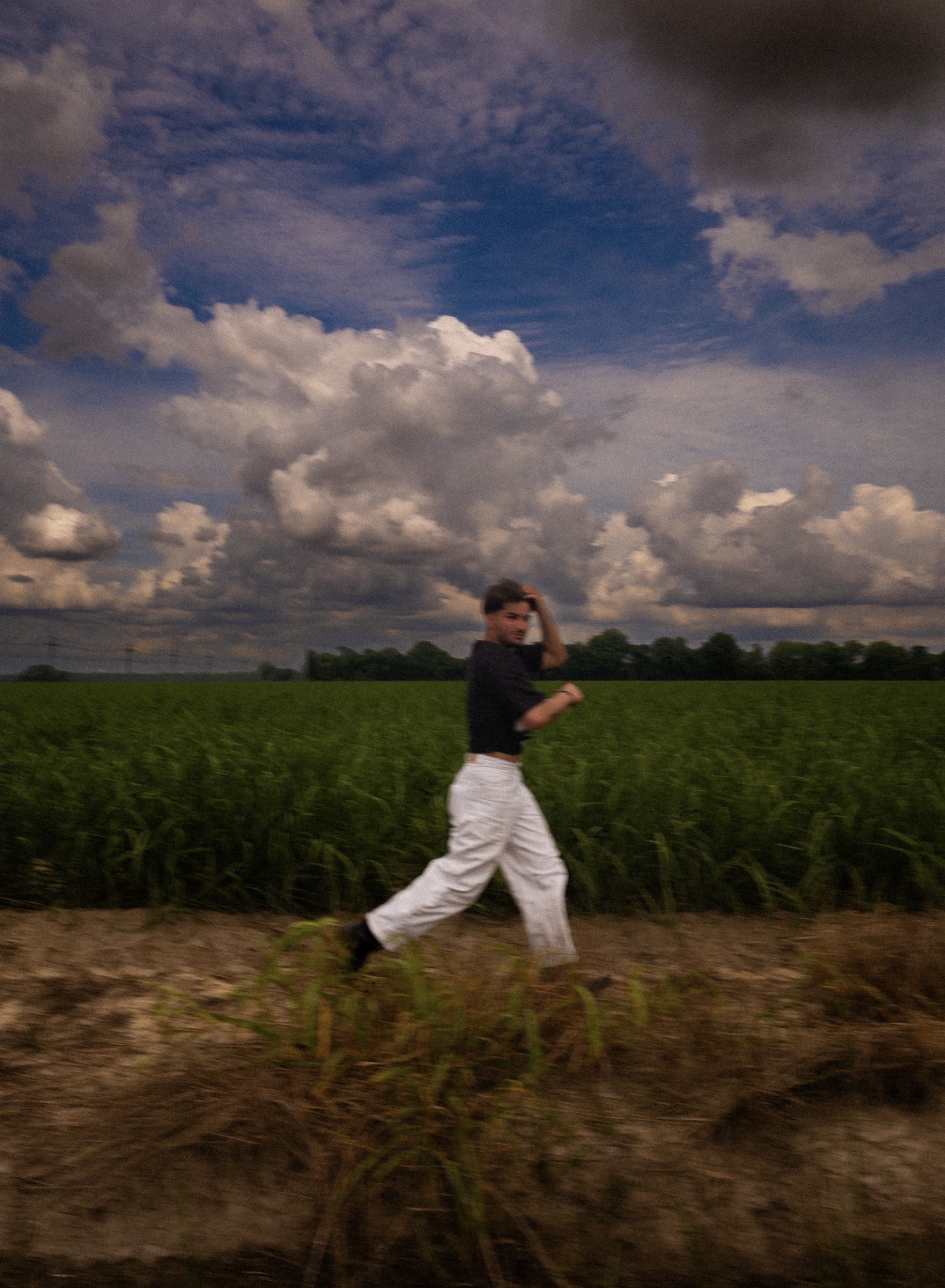 Child walking along a dirt path with green fields and a cloudy sky in the background.