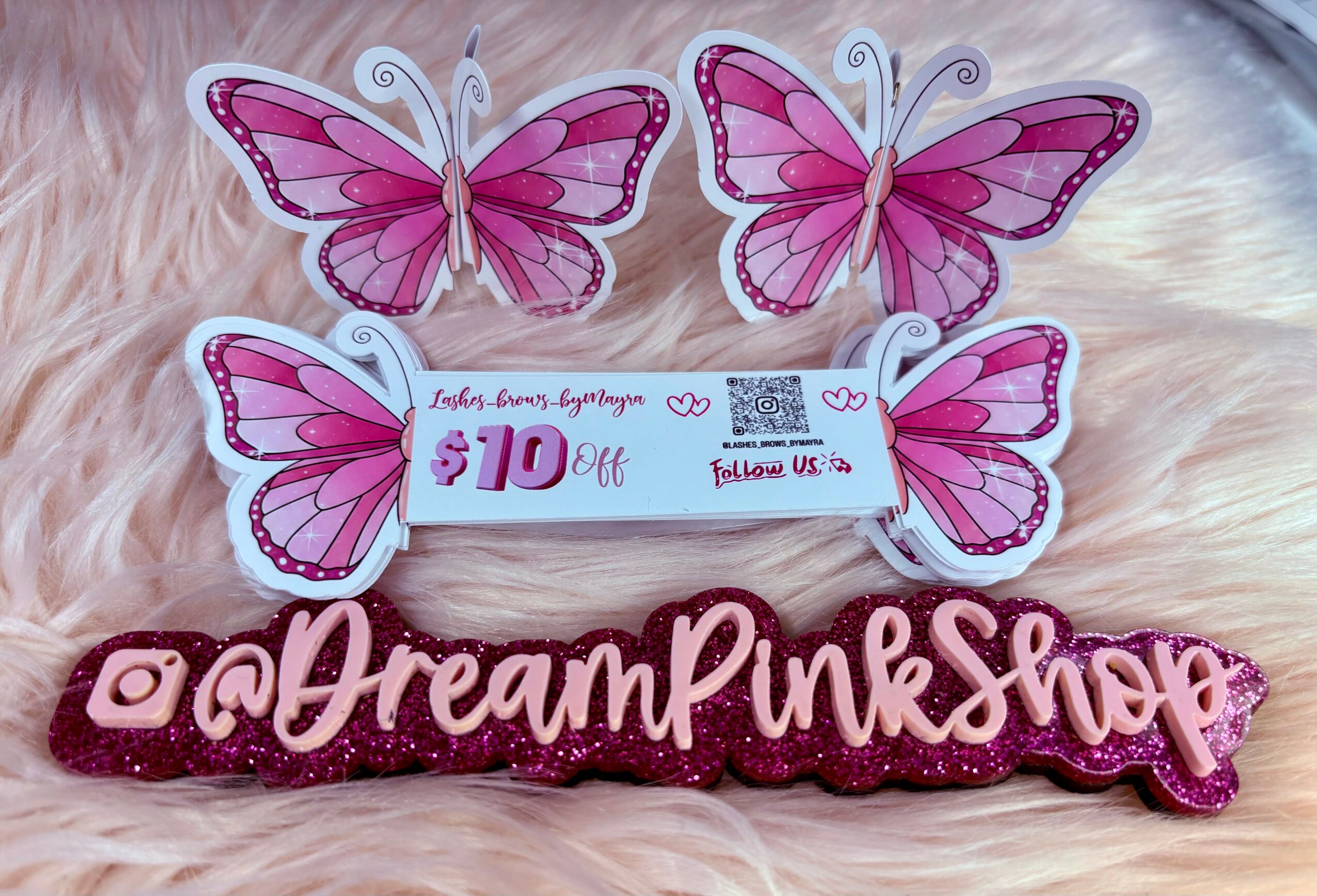 Decorative pink butterfly cutouts, a coupon for $10 off, and a pink sign reading 'a Dream Pink Shop' on a soft surface.