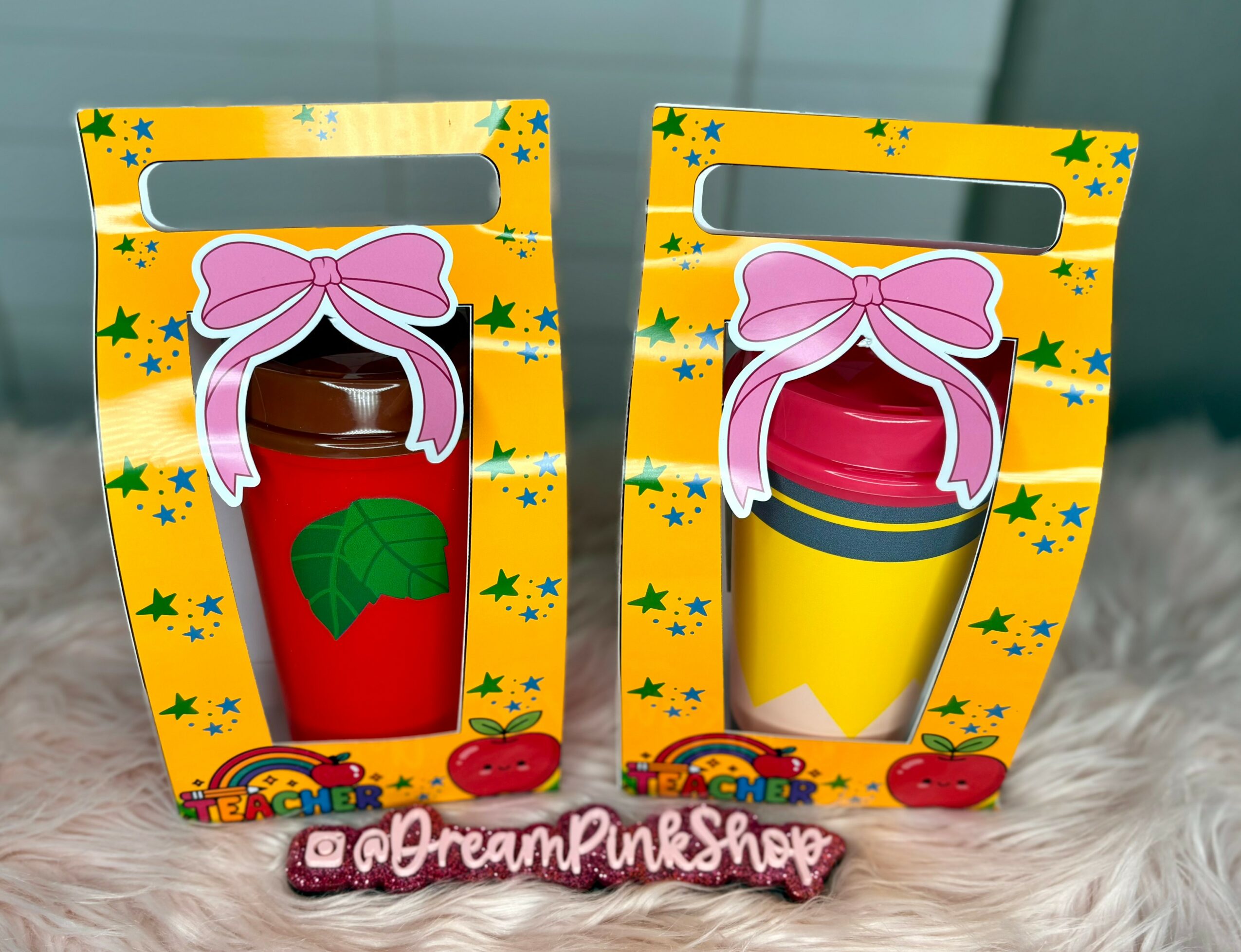 Two colorful toy drink containers in yellow boxes with star patterns, pink bows, and fruit illustrations, placed on a soft surface.