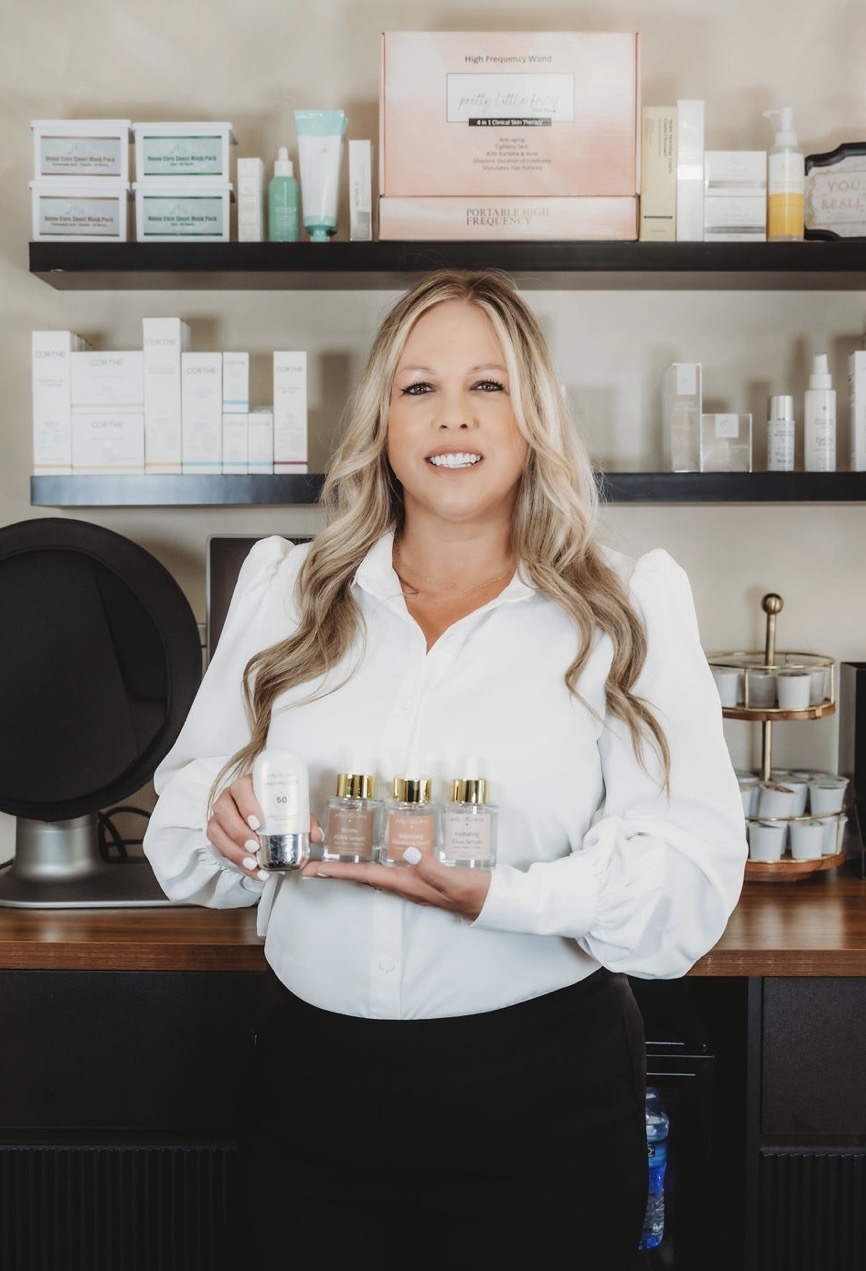 Woman with long blonde hair holding skincare products in a store, shelves with skincare items behind her.