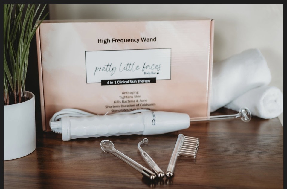 A high frequency wand device and attachments on a wooden surface with a pink box labeled 'pretty little faces' behind them.