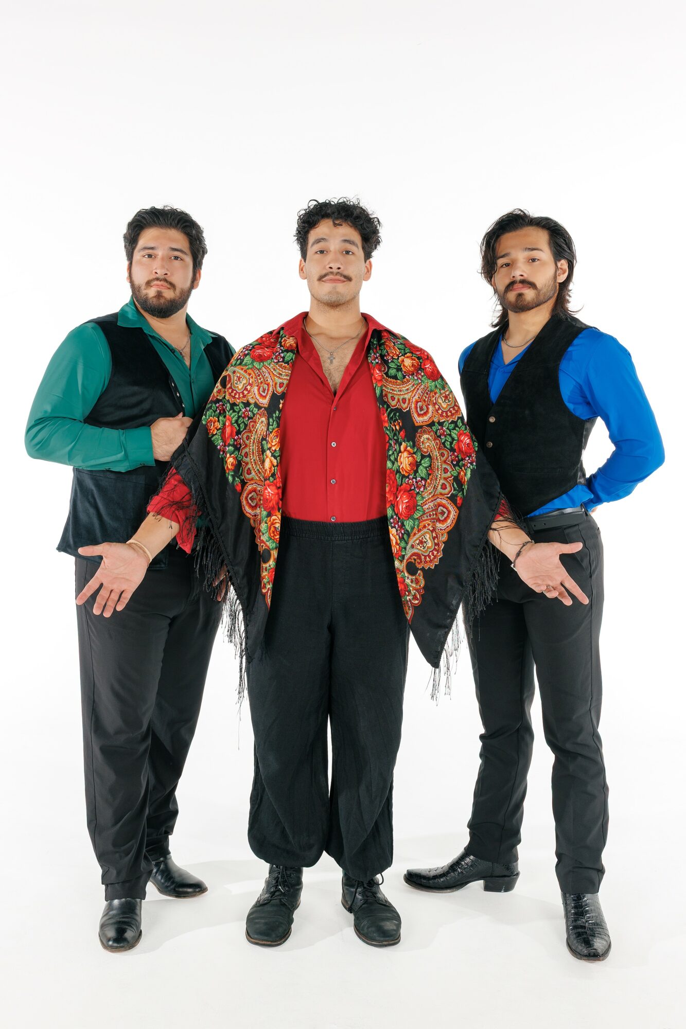 Three men stand together, wearing colorful shirts and vests, with a plain white background.