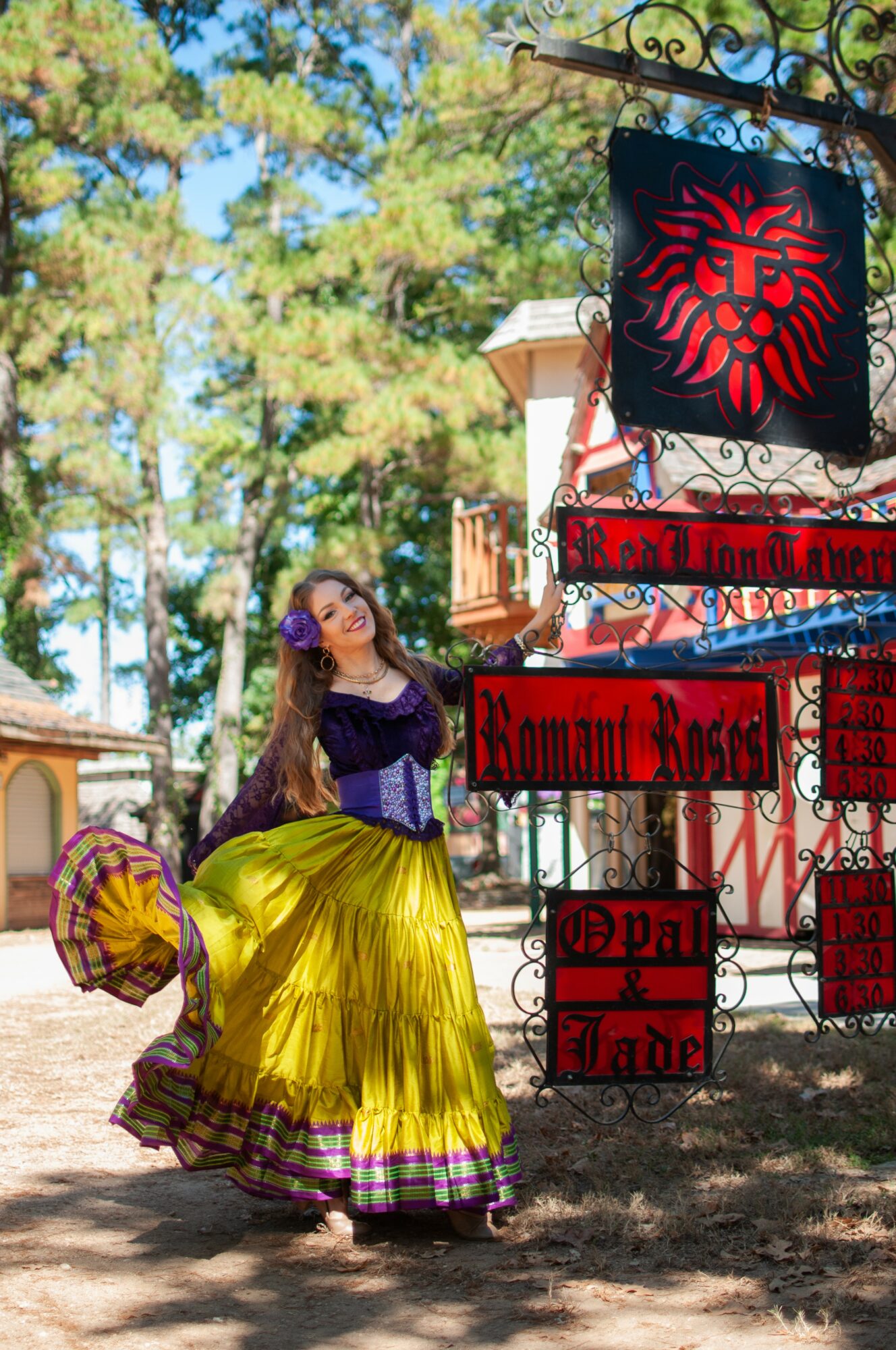 Woman in colorful dress standing outdoors near decorative signs, trees in background, sunny day.