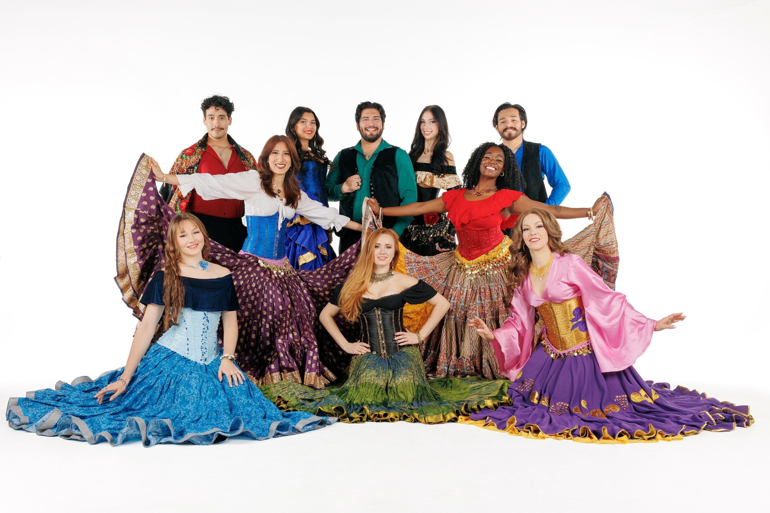 Group of nine people in colorful costumes, some sitting and some standing, posing against a white background.
