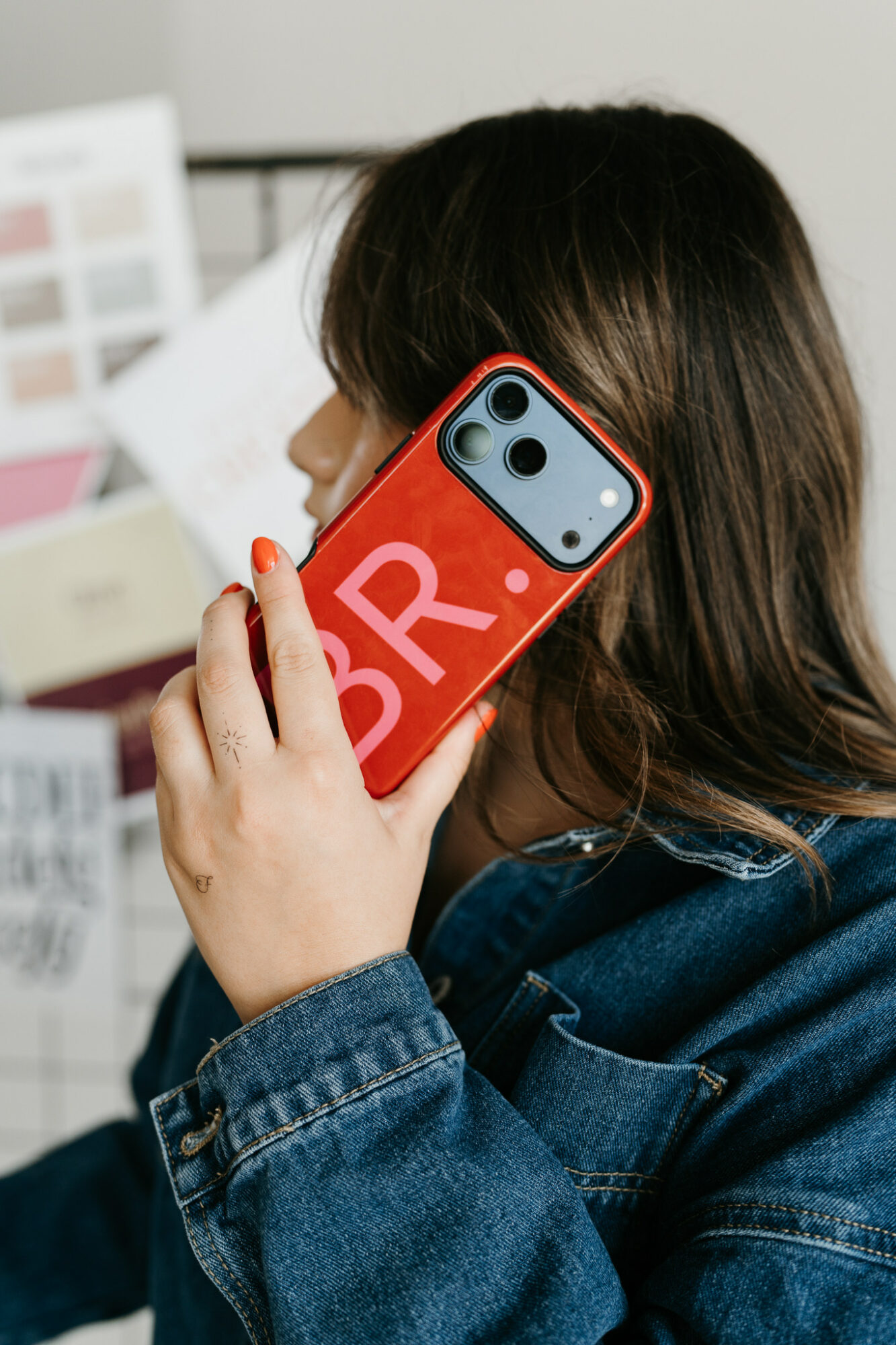 Person holding a smartphone with a red case and large white letters, face partially visible, in an indoor setting.