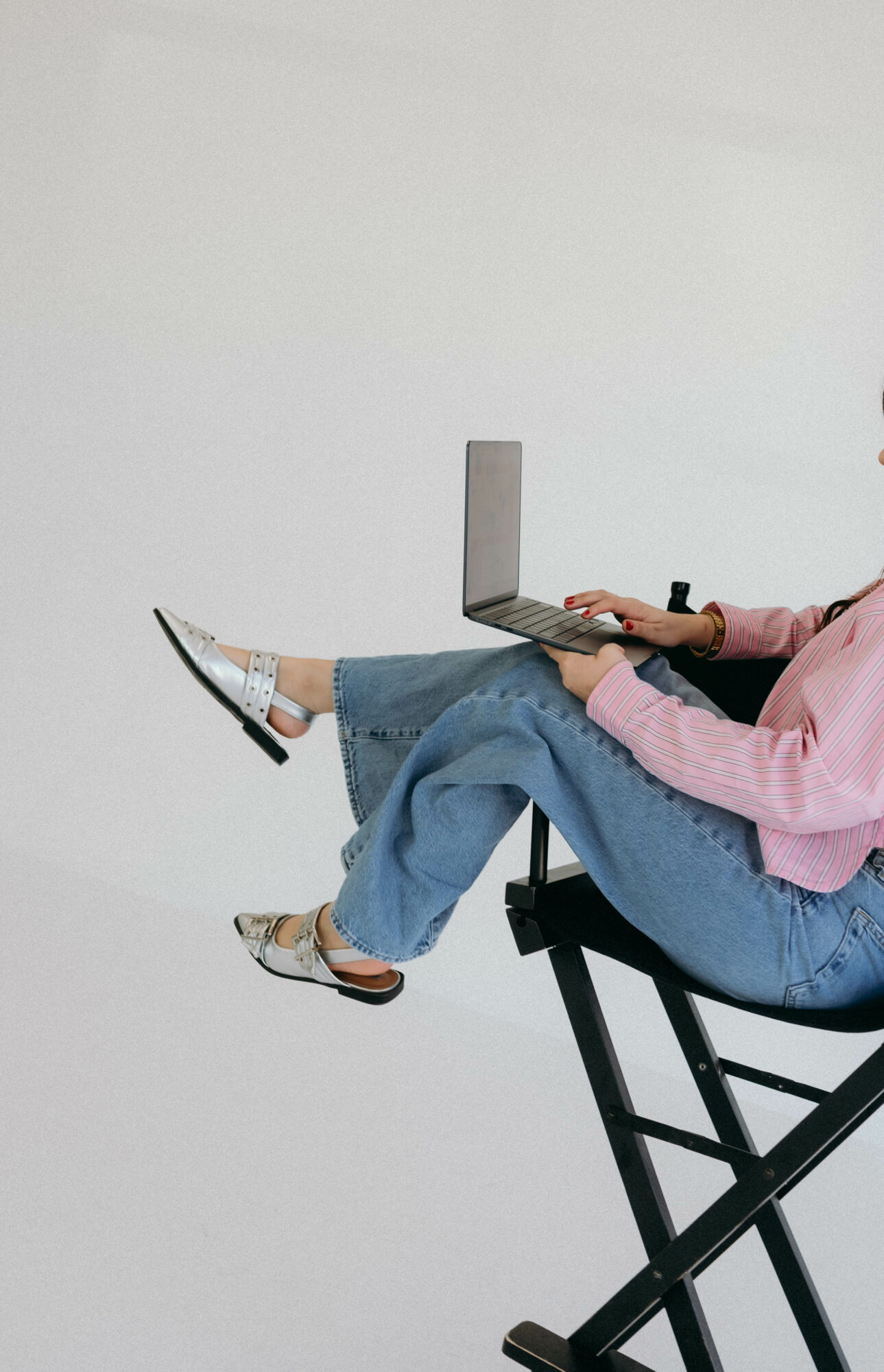 Person sitting on a chair using a laptop, legs extended and crossed, against a plain white background.